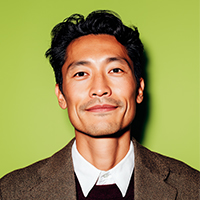 Smiling Asian man in a brown blazer and white collared shirt against a green background.