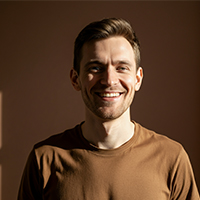 Smiling man with short brown hair wearing a brown shirt against a brown background.