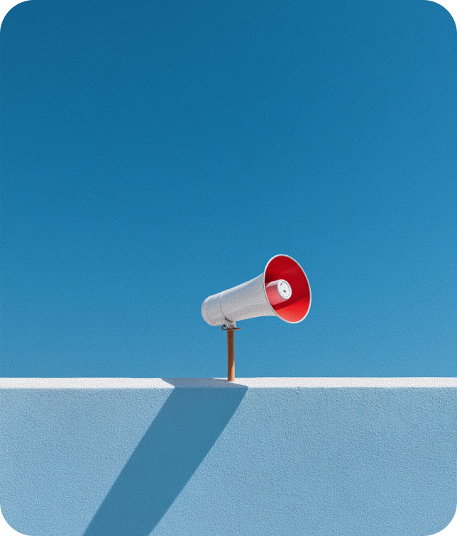 White and red megaphone mounted on a white wall casting a long shadow under a clear blue sky.
