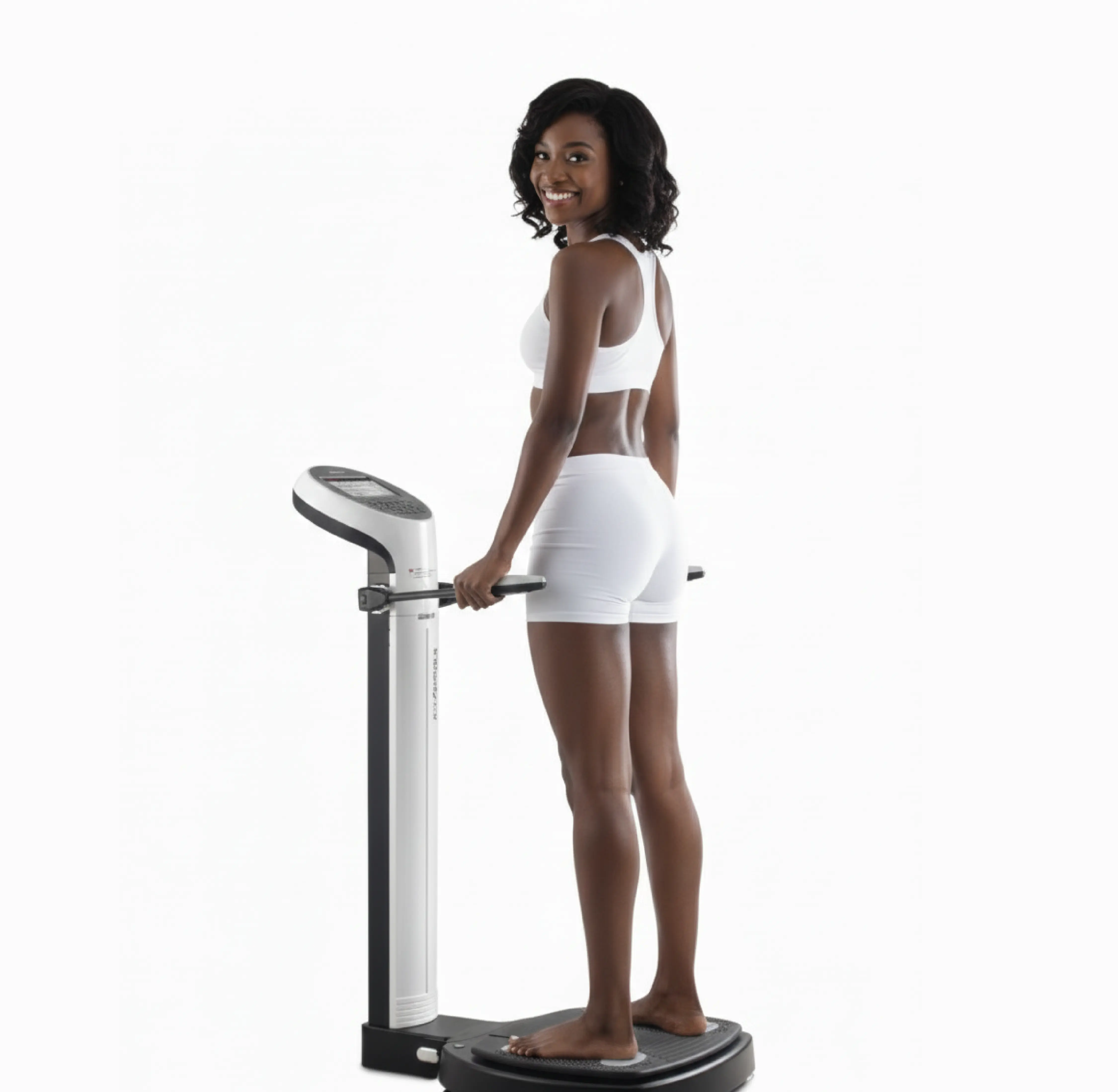 Smiling woman in white workout attire standing barefoot on a body composition analyzer machine.