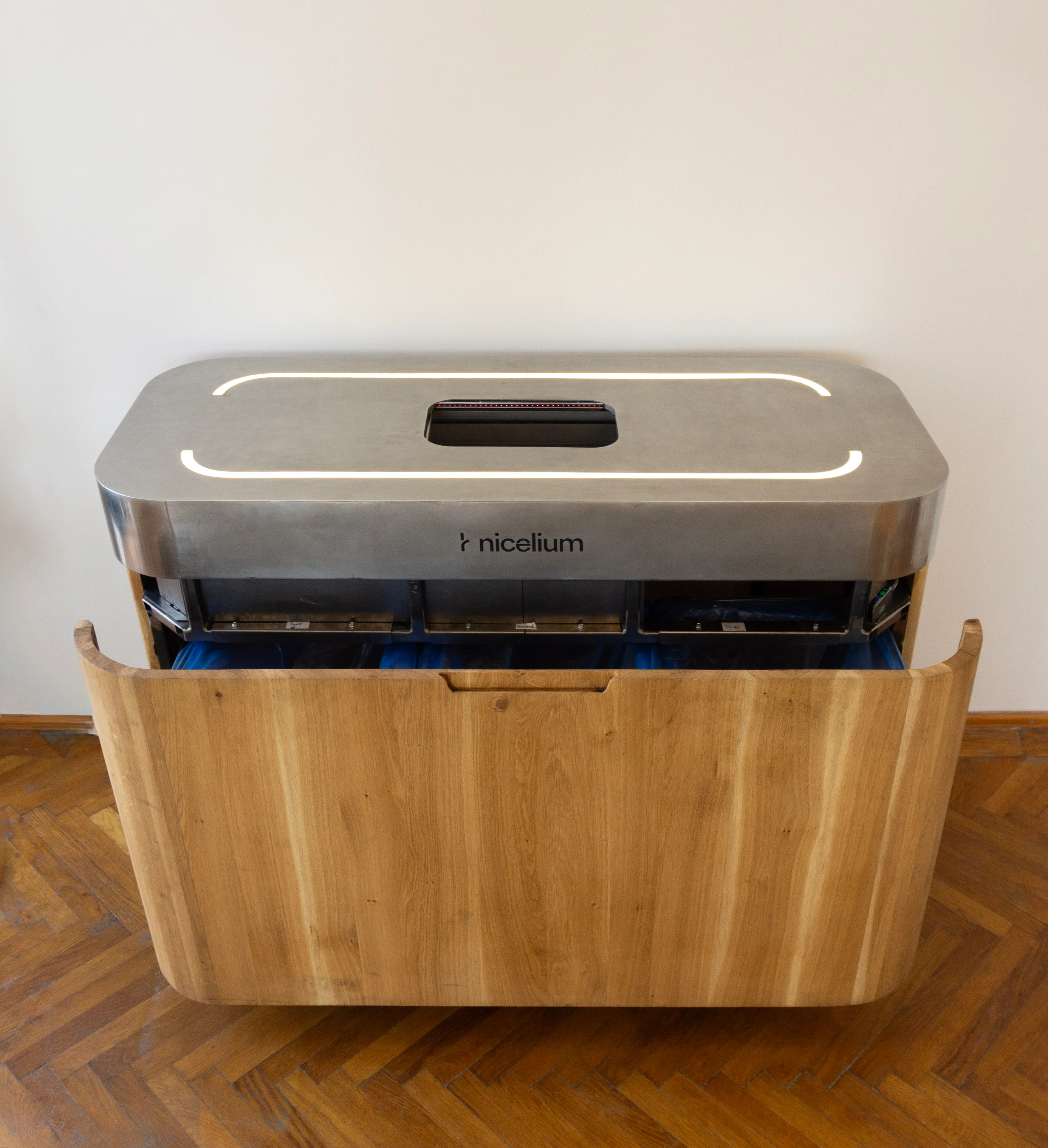 Modern Nicelium waste sorting station with stainless steel top and wooden front panel on parquet floor.