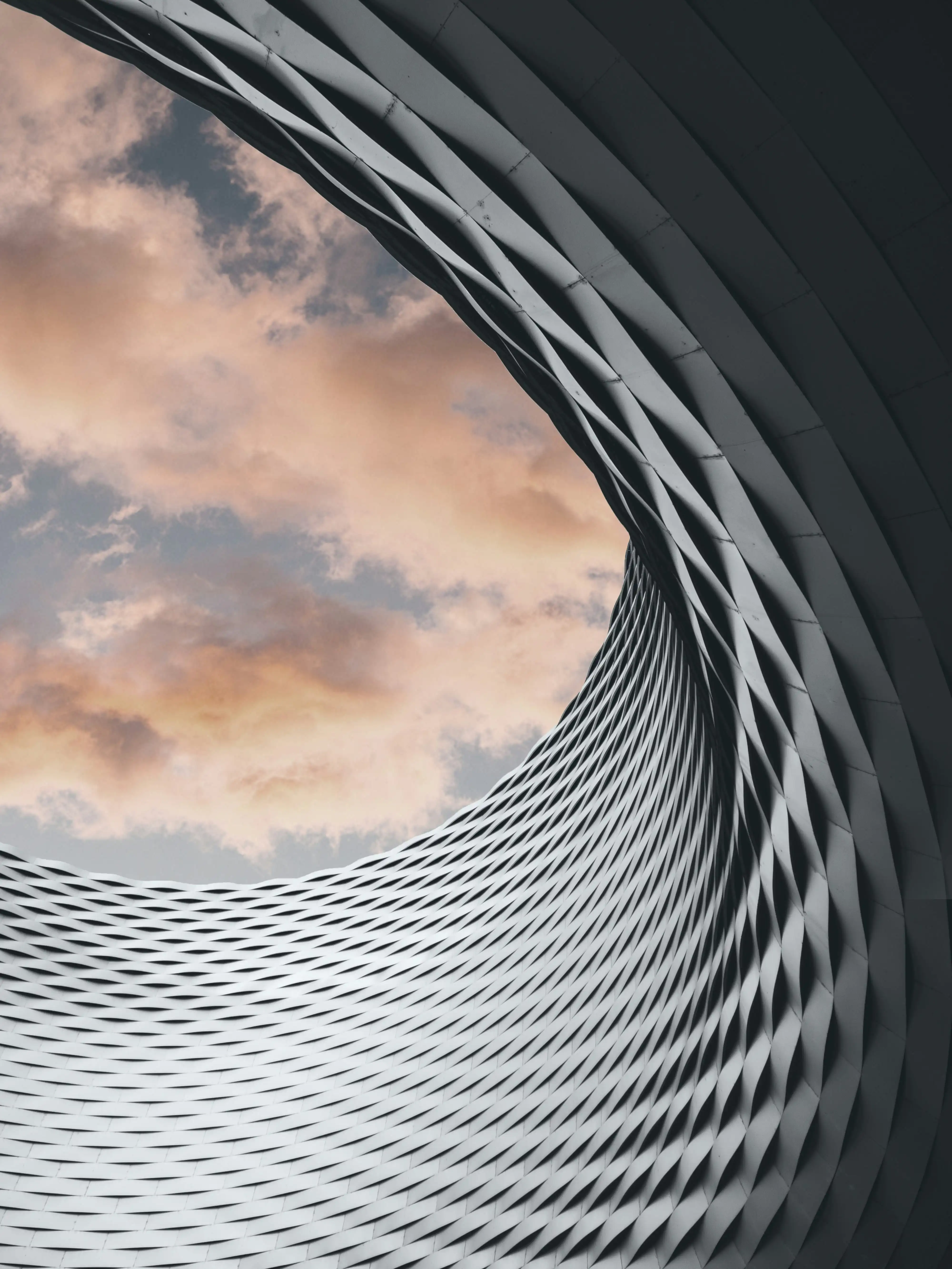 Vue en contre-plongée d'une structure architecturale en forme de vortex avec un ciel nuageux en arrière-plan.
