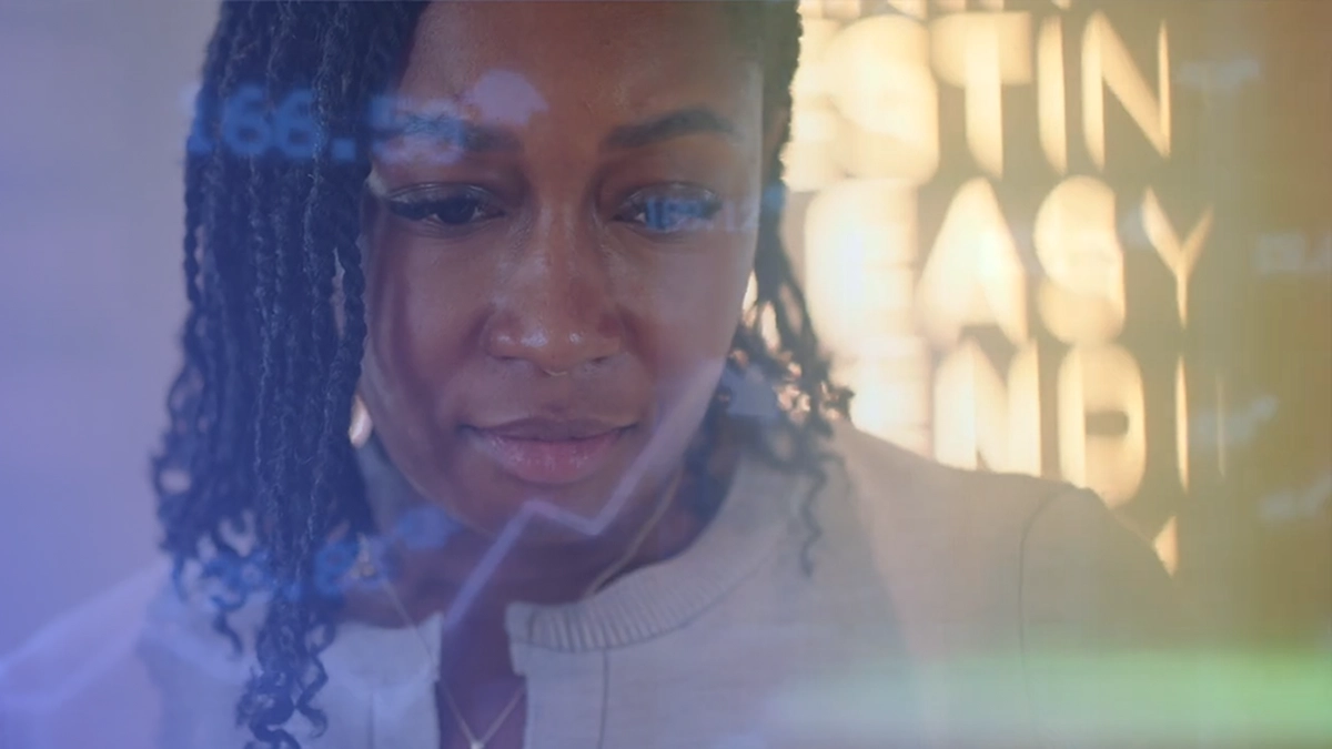 Close-up of a woman with braided hair looking thoughtfully at a translucent screen displaying financial graphs and text.