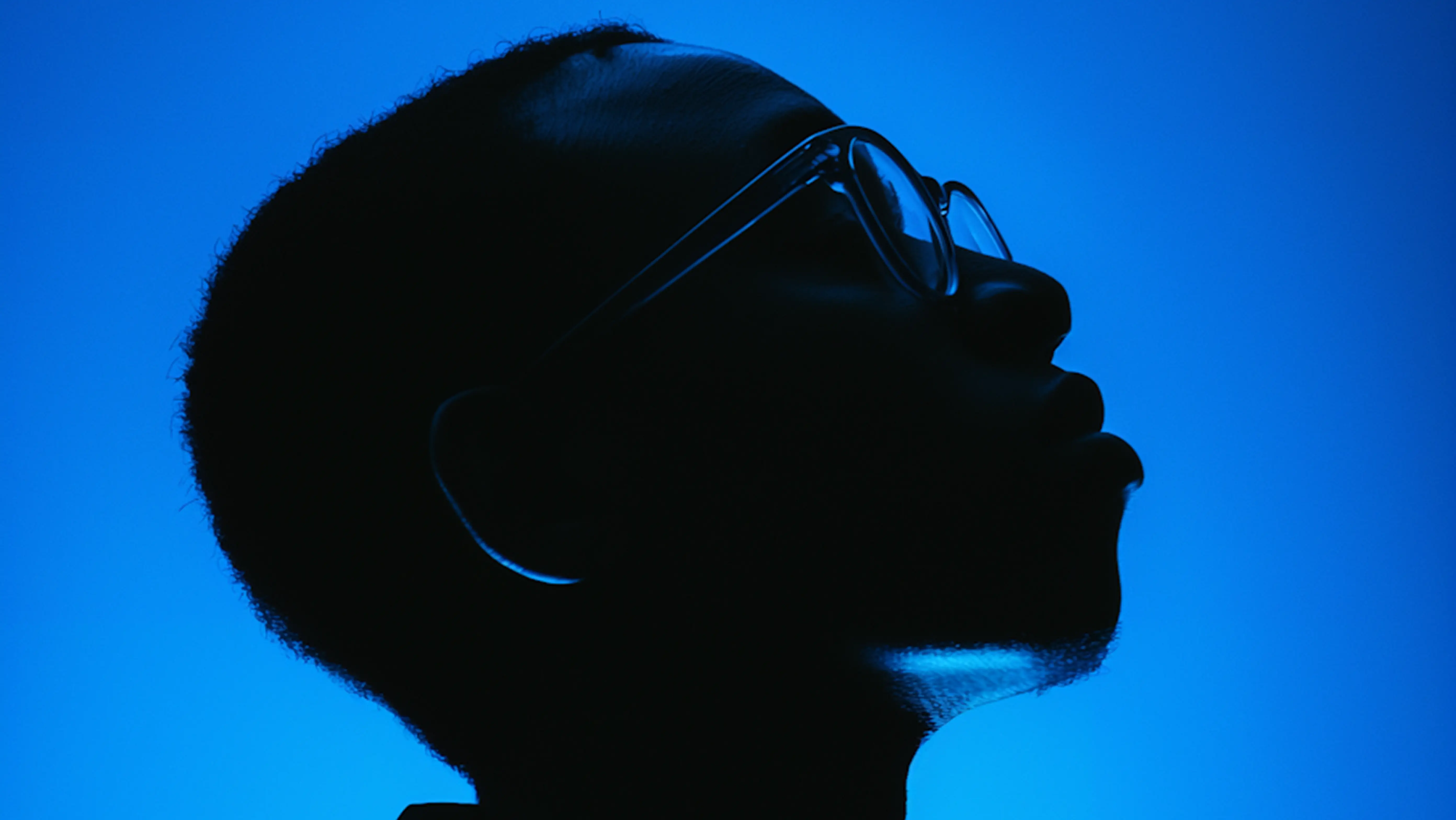 Silhouette of a person wearing glasses against a blue background.