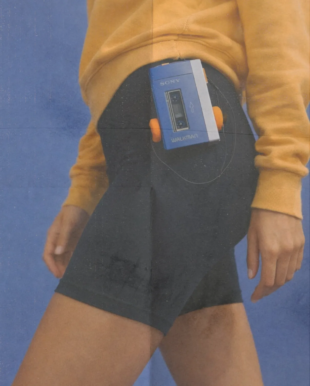 Active lifestyle portrait with retro portable music player clipped to athletic shorts. Casual sportswear against a blue studio background, movement and fitness energy. Vintage tech aesthetic combined with wellness, exercise, motivation, training routine and modern healthy lifestyle concept.
