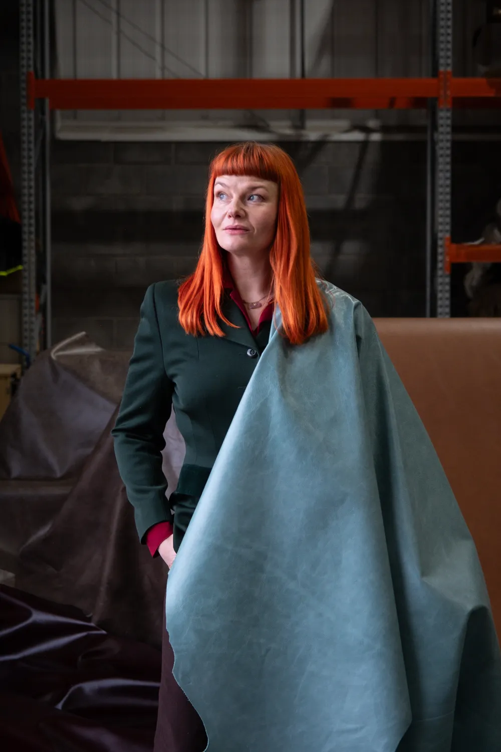 Woman with bright orange hair holding a large piece of light blue fabric in an industrial setting.