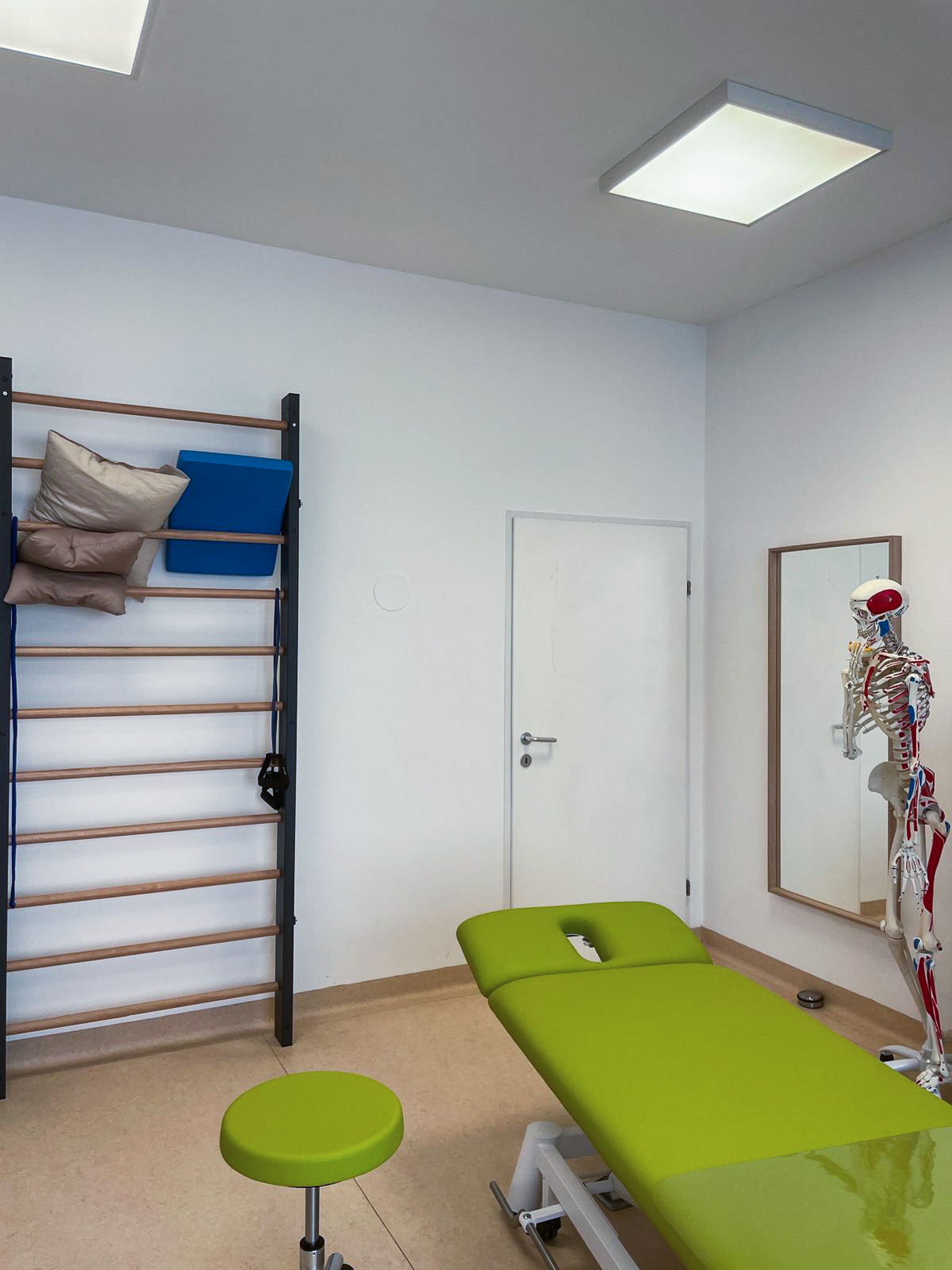 Bright room with exercise ball, yoga mat, dumbbells, and massage table near large windows.