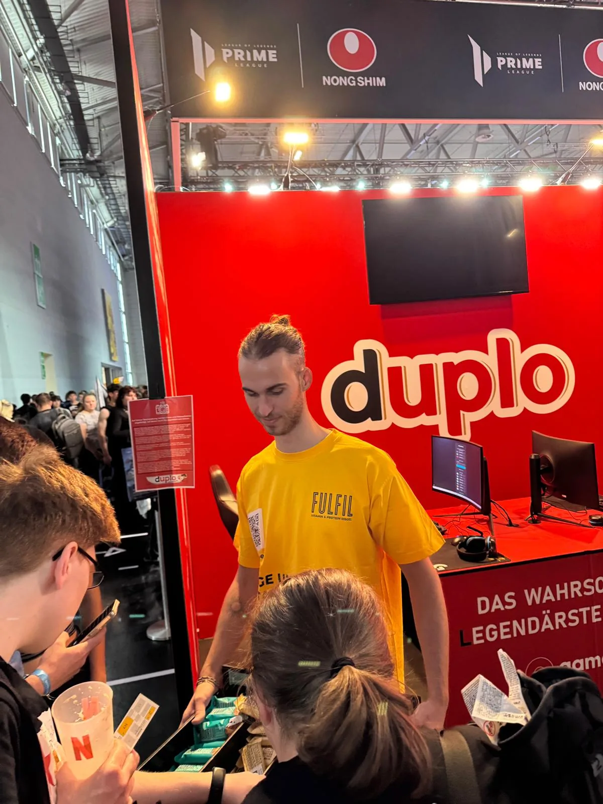 Mitarbeiter im gelben Shirt im Gespräch mit Besuchern am duplo-Stand auf der gamescom 2026 in Köln