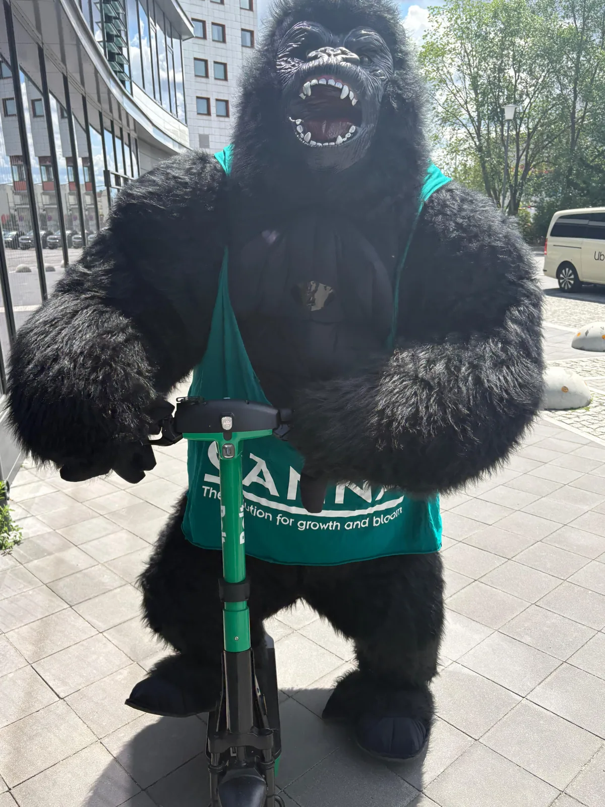 Walking-Act-Gorilla im CANNA-Shirt steht mit einem grünen E-Scooter vor einem Gebäude in Berlin