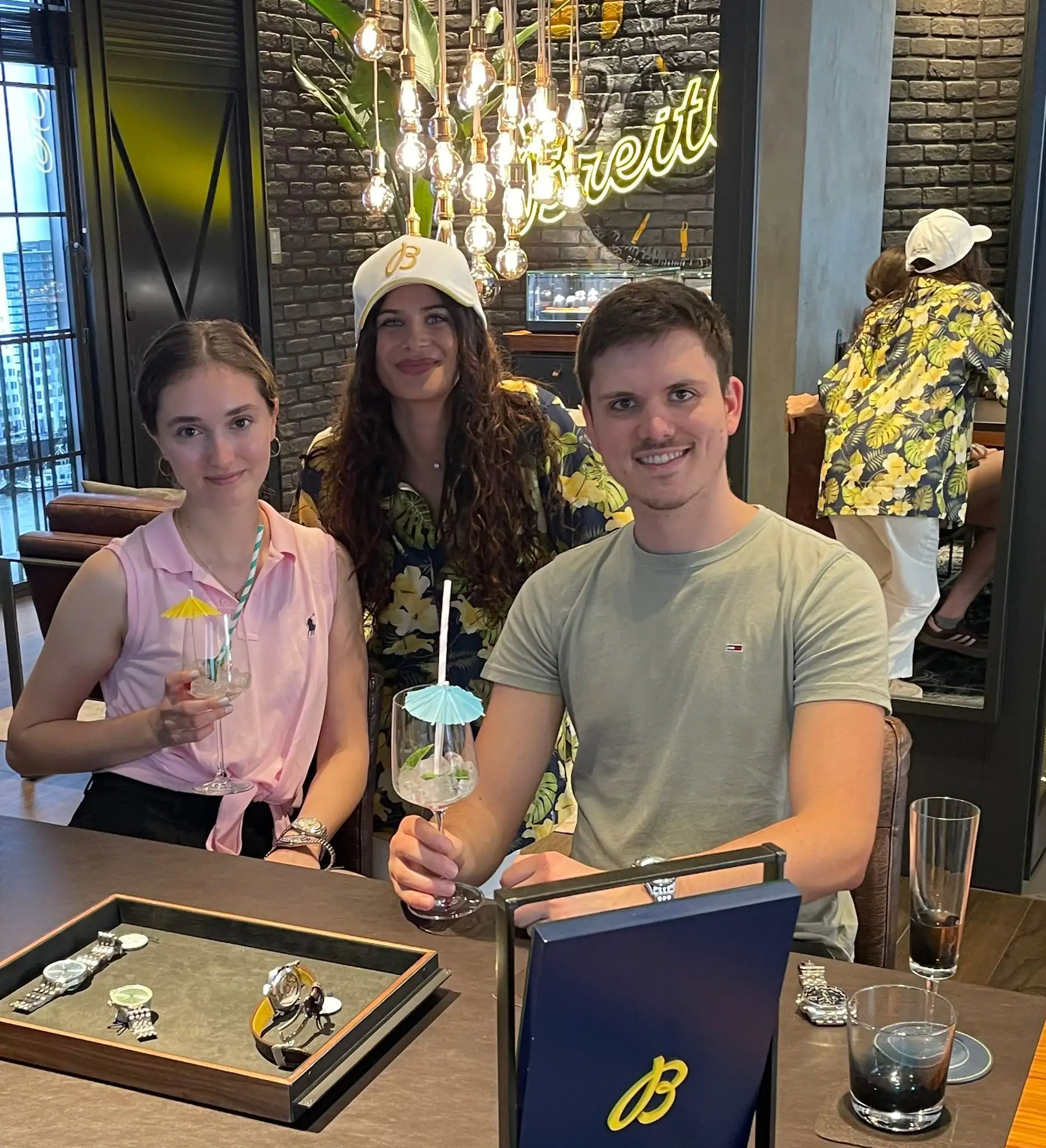 Three guests and hosts with cocktails and paper umbrellas at the counter inside the Breitling Boutique Düsseldorf