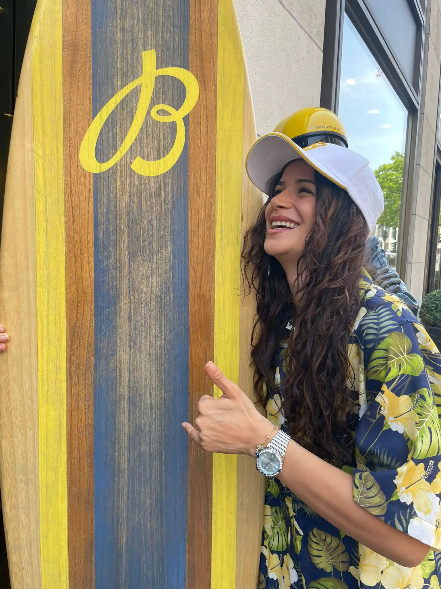 Hostess in a Hawaiian shirt and Breitling cap laughing next to a surfboard with the Breitling logo outside the boutique on Königsallee