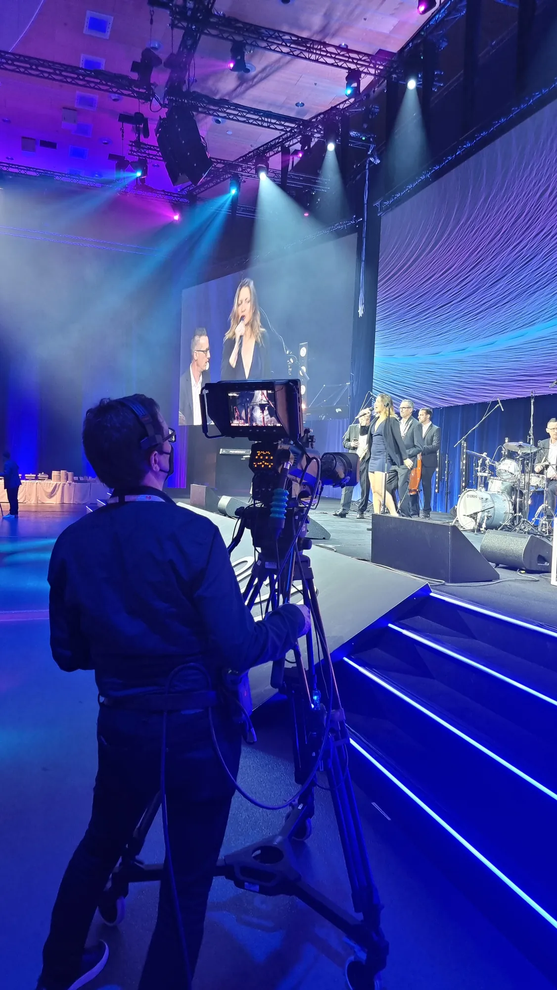 Videographer with camera in front of the stage with singer and band at the Huawei IDI Forum 2022 | eventas