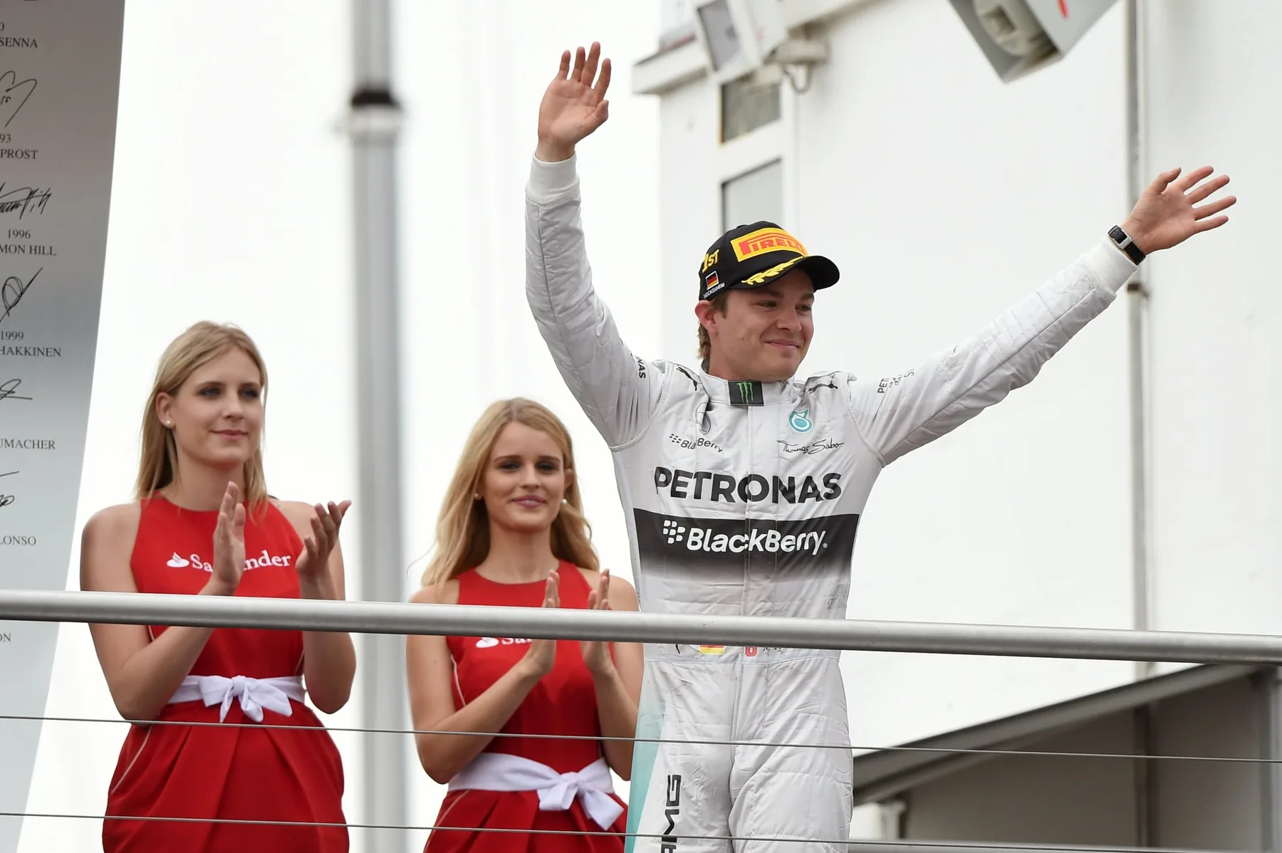 Nico Rosberg waves from the podium after his win while two grid girls in red Santander dresses applaud