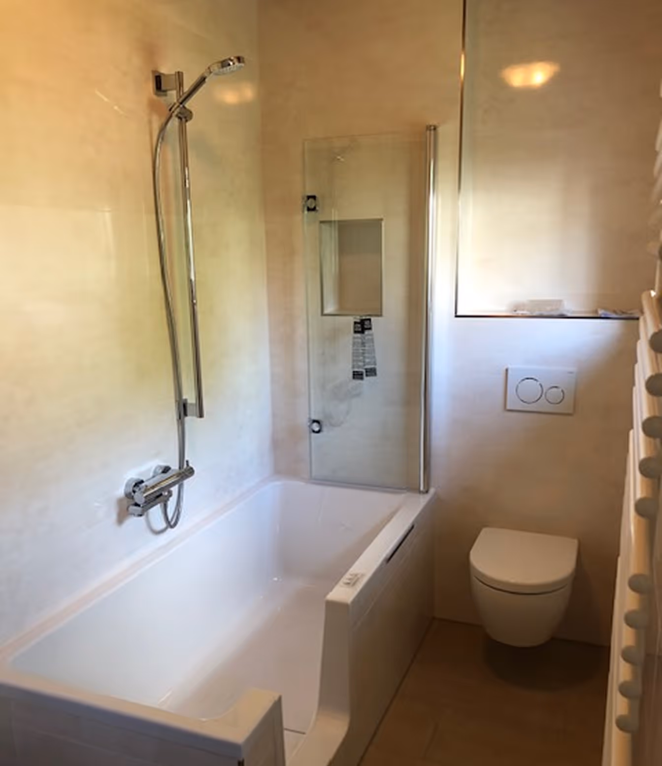 Moderne Badezimmer mit einer weißen Badewanne mit Duschkopf und einer Wandtoilette mit Spülknöpfen.