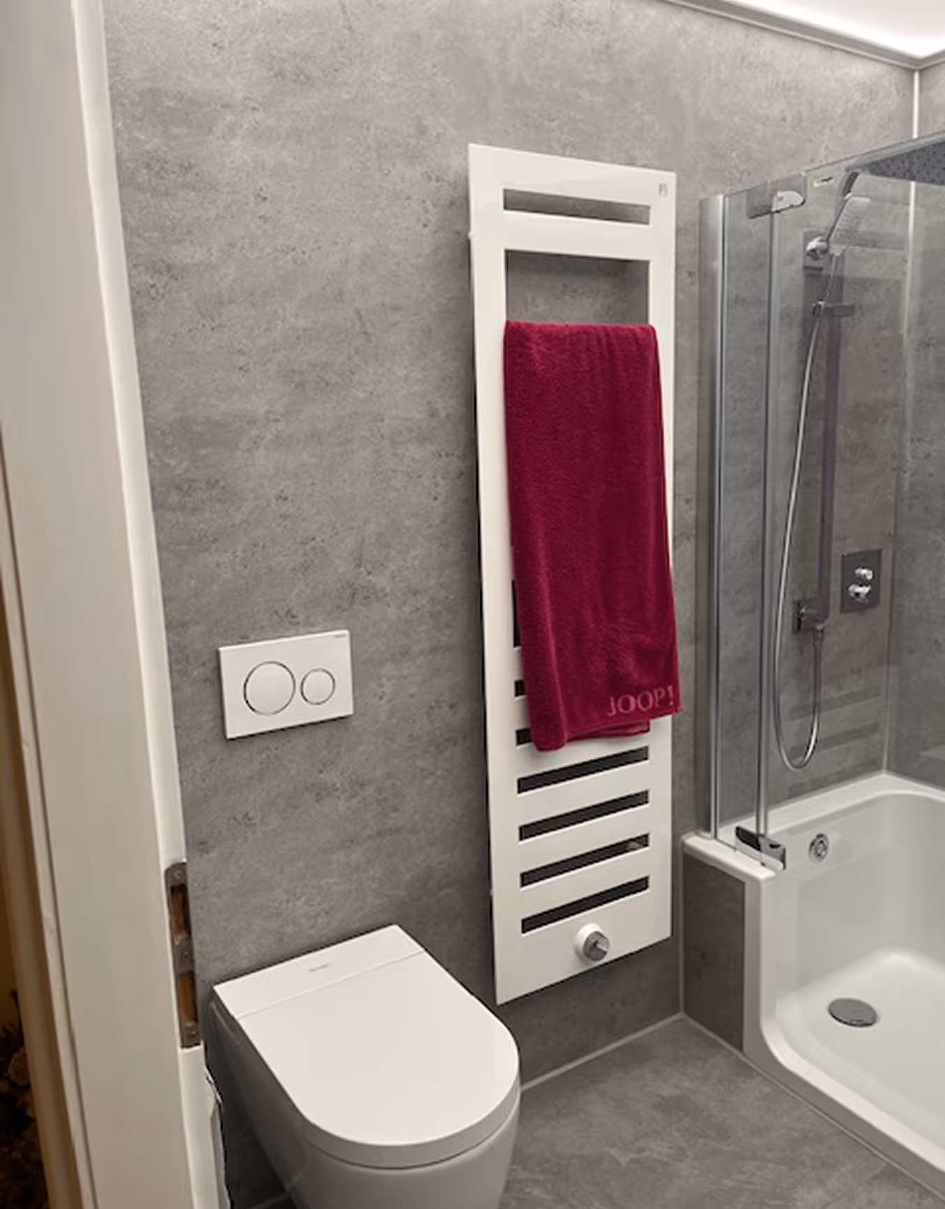 Modernes Badezimmer mit weißem WC, Handtuchwärmer mit rotem Handtuch und Dusche mit Glaswand.