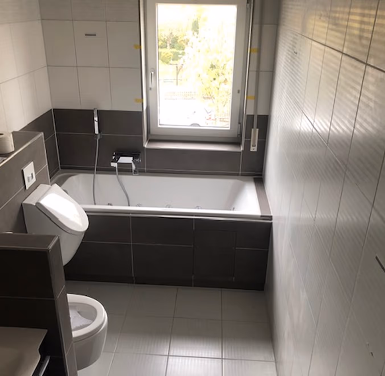 Modernes Badezimmer mit Badewanne unter einem Fenster und Toilette neben einer halben Wand.