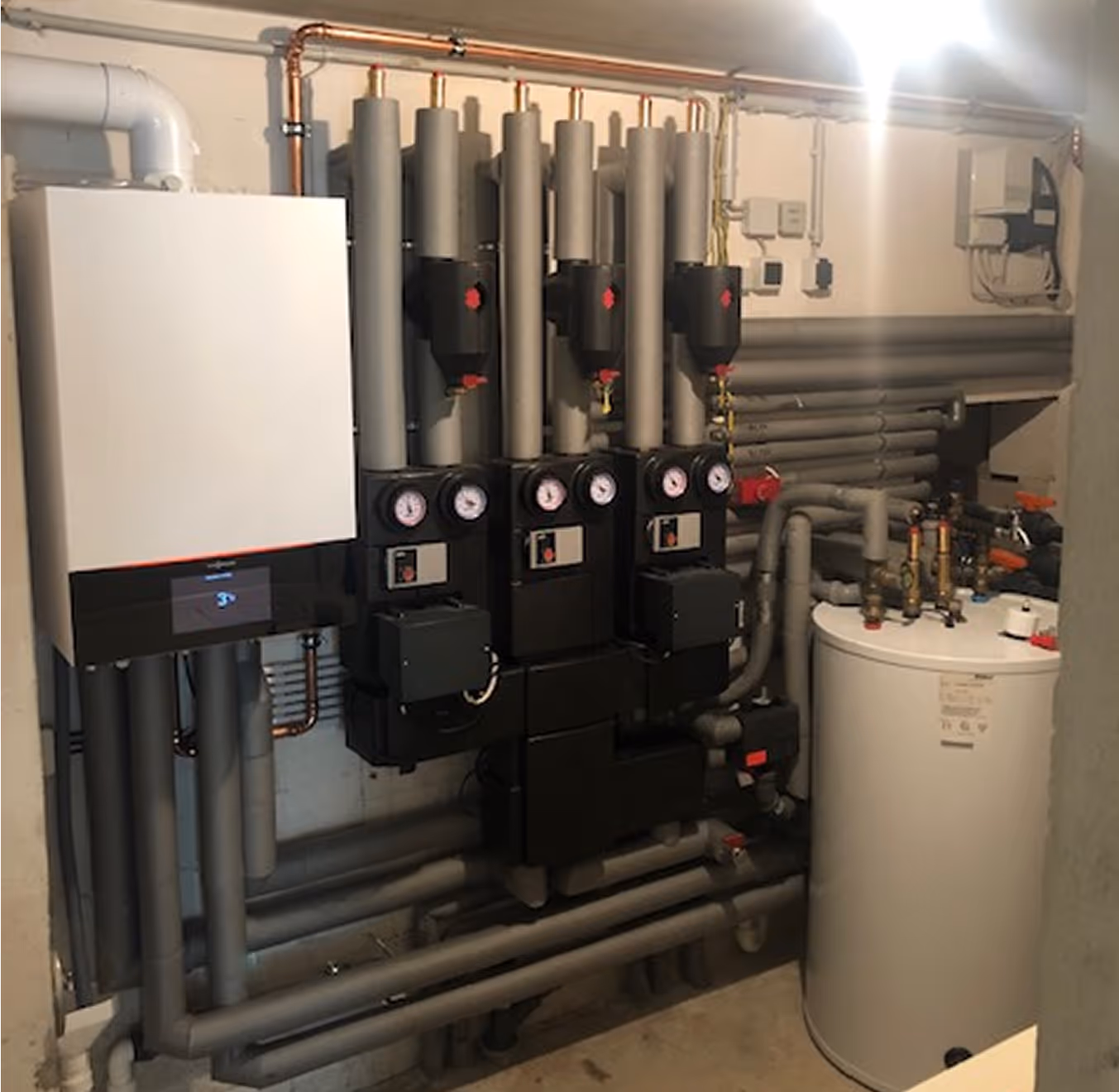 Heizungsanlage mit Rohrleitungen, Druckmanometern und Warmwasserspeicher in einem Technikraum.