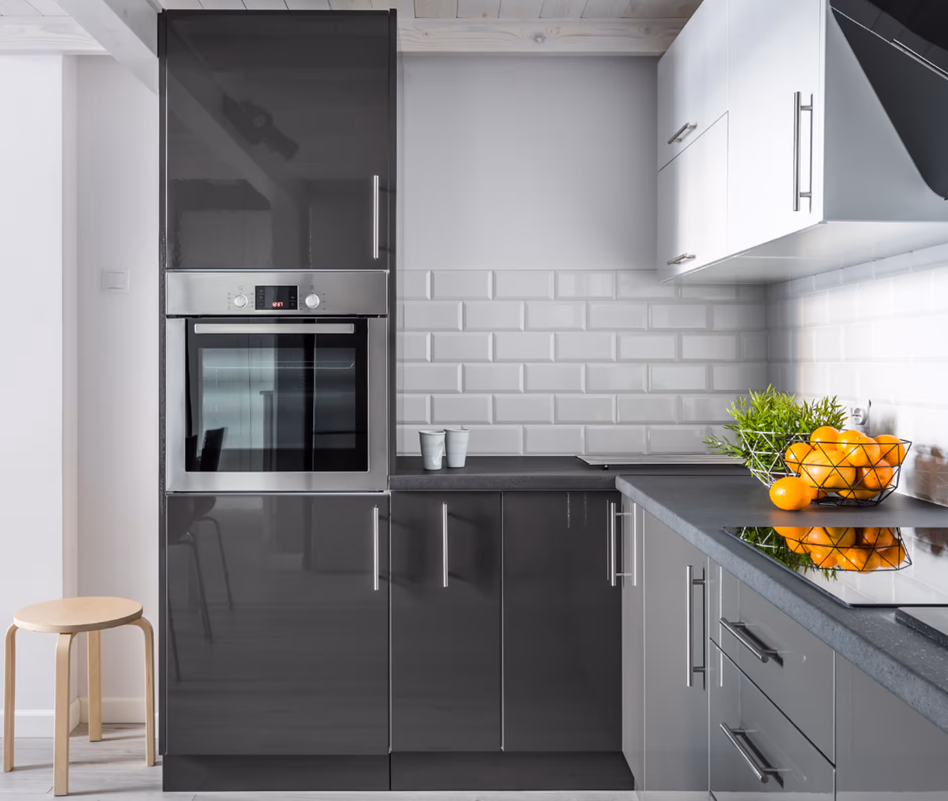 Moderne Küche mit grauen Hochglanzschränken, Edelstahl-Backofen, weißen Fliesen, Korb mit Orangen und grünen Pflanzen.