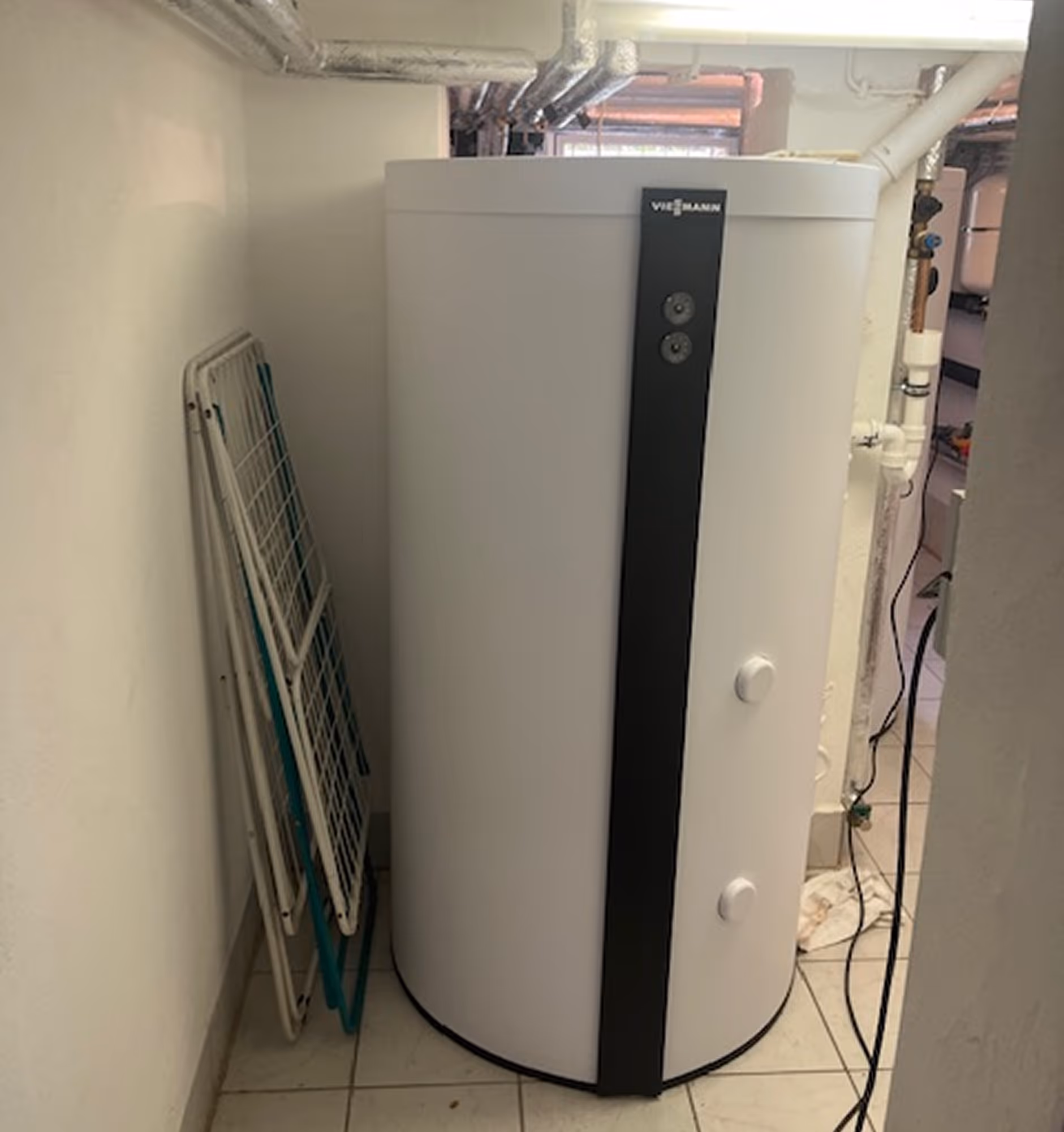 Großer, zylinderförmiger Heizkessel mit der Aufschrift Viessmann in einem Kellerraum neben zusammengeklappten Wäscheständern.