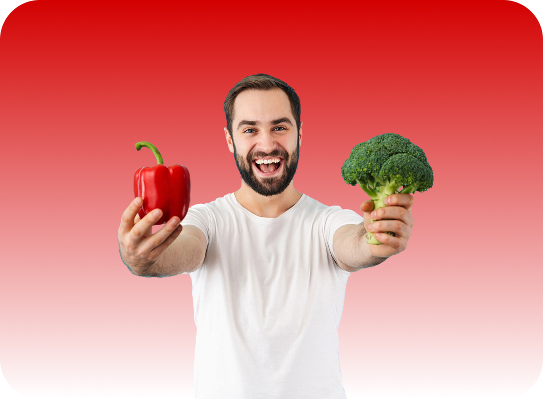 Man with beard smiling and holding a red bell pepper and broccoli against a red gradient background.