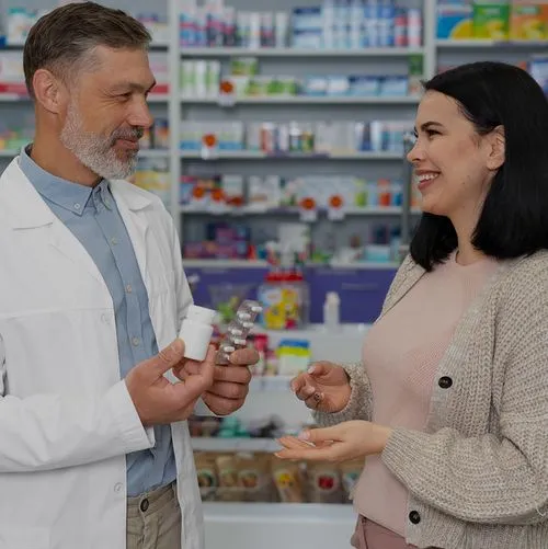Pharmacist in white coat explaining medication to a smiling woman in a pharmacy.