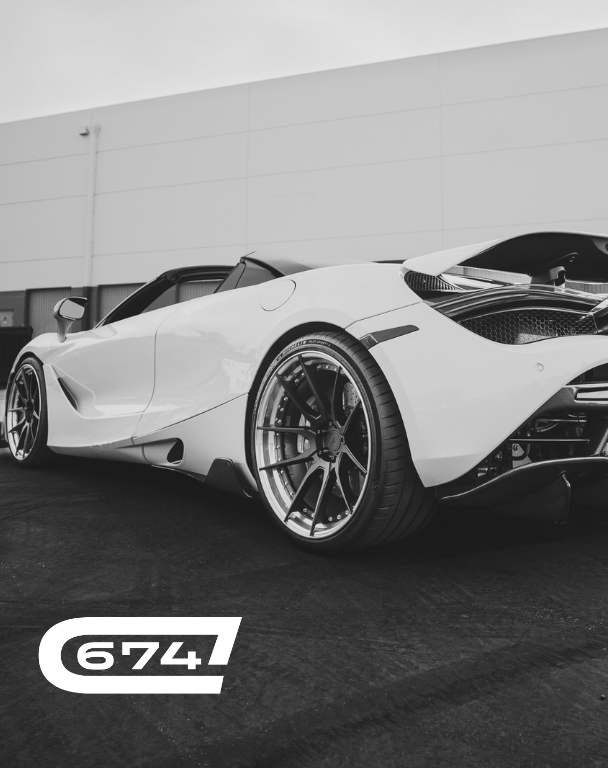 Rear-side view of a sleek white sports car parked on dark pavement near a building.