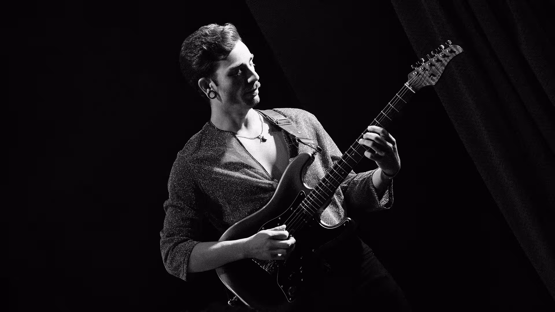 Black and white photo of a man playing an electric guitar against a dark background.