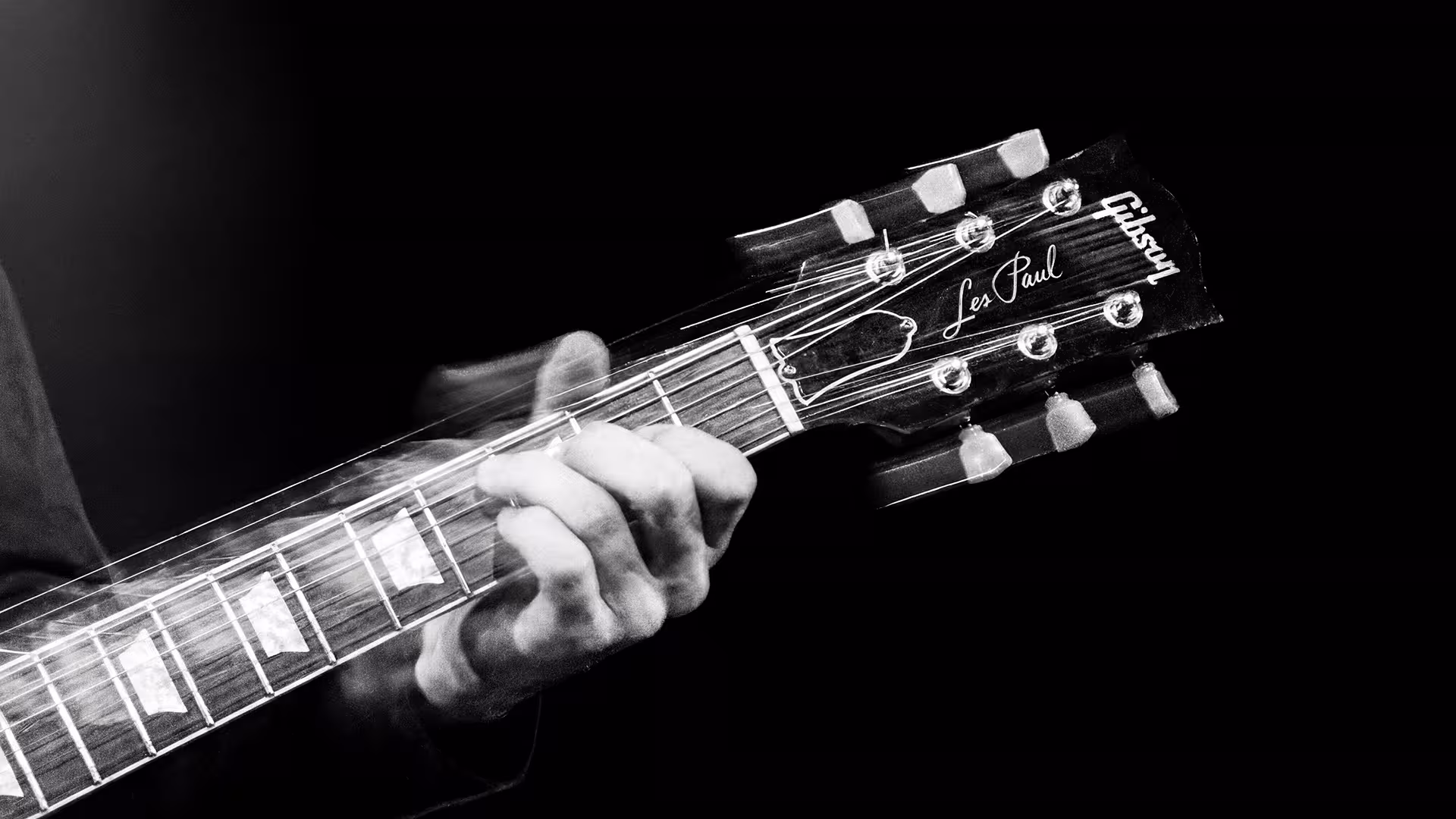 Black and white photo of a hand playing a Gibson Les Paul guitar neck and headstock.