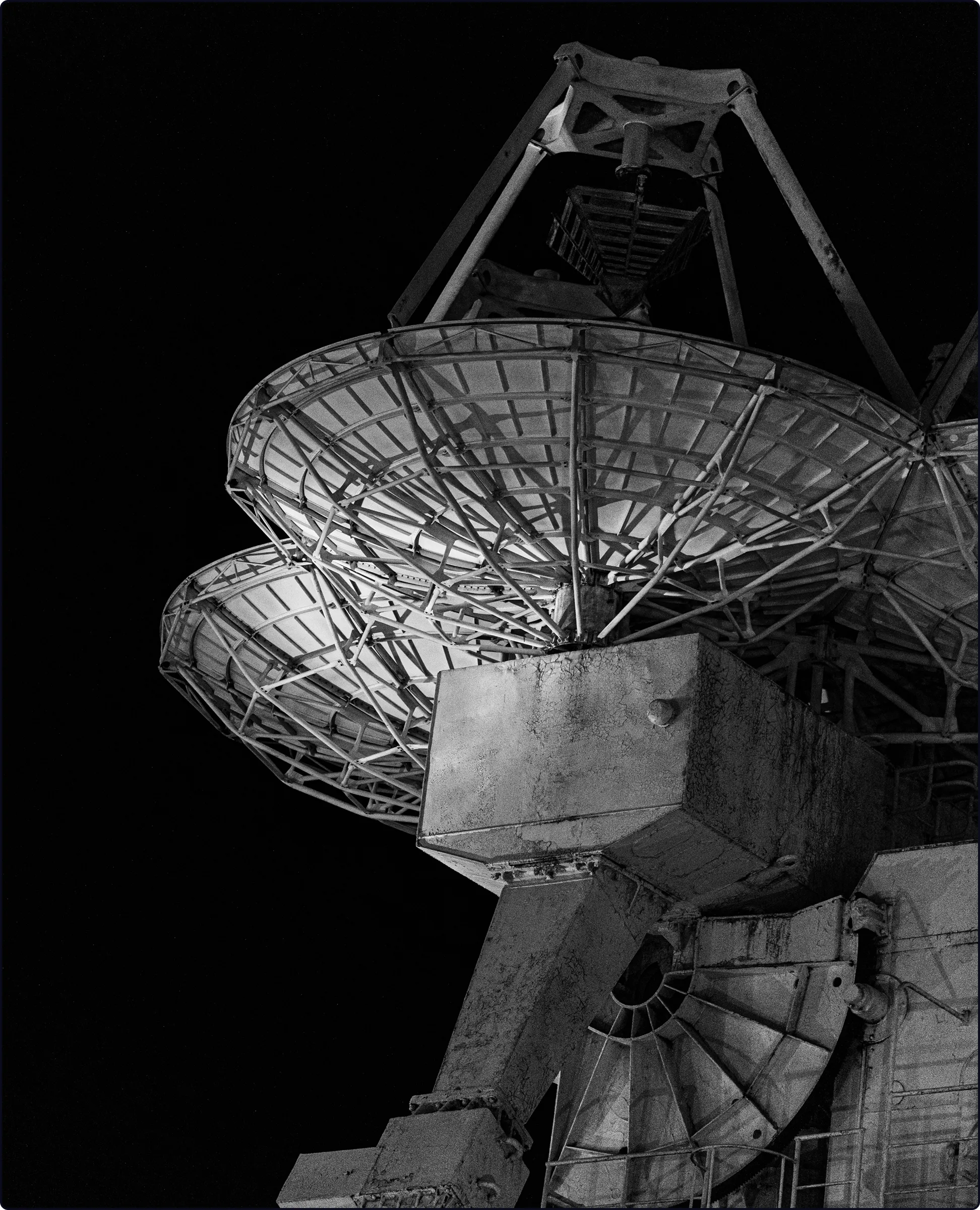 Close-up black and white photo of large satellite dishes against a dark sky.