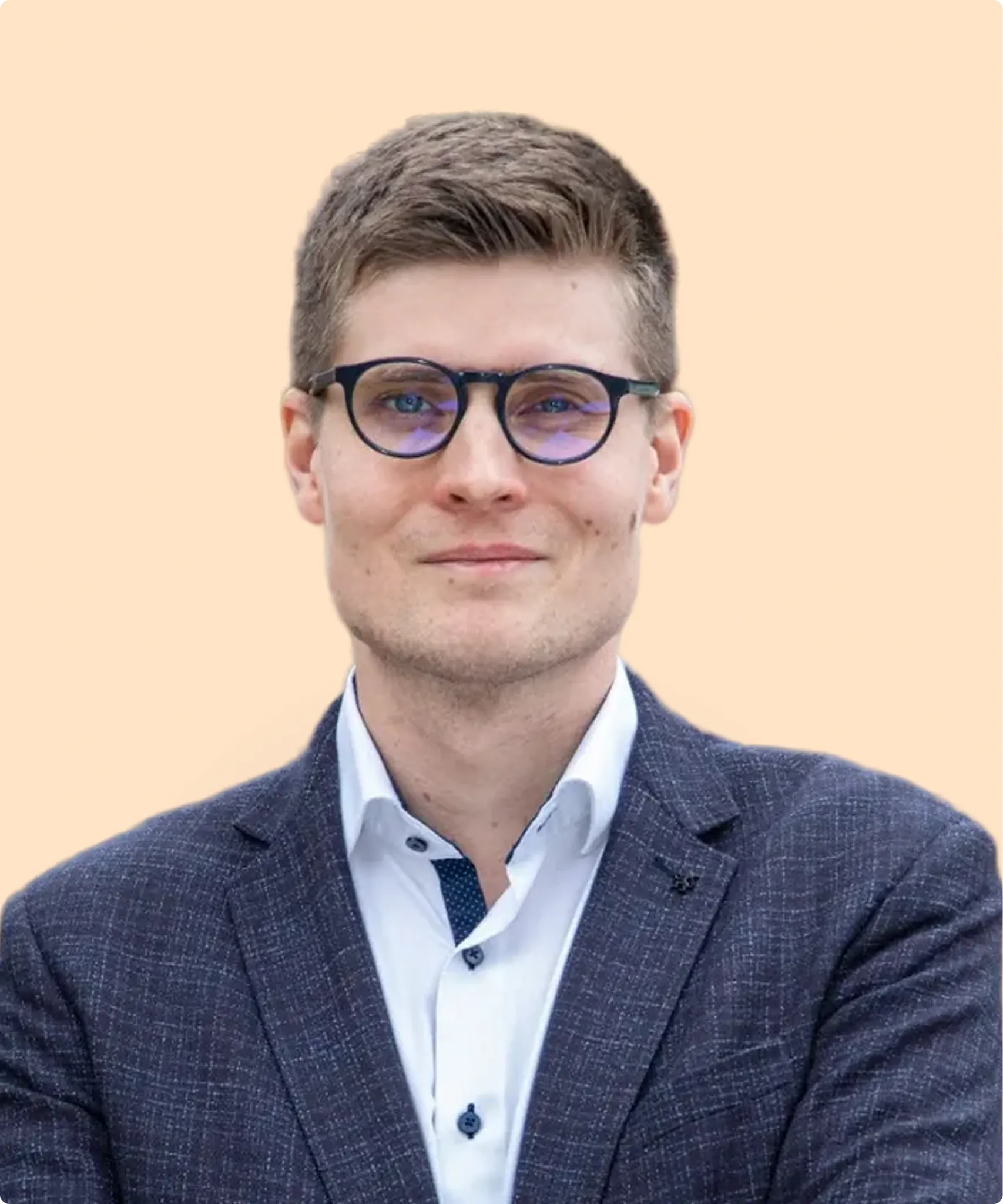 Man with short brown hair wearing round glasses, a white shirt, and a dark checked blazer against a peach background.