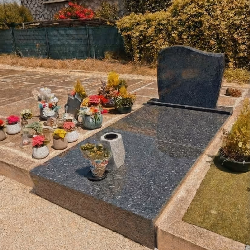 Smiling elderly man with glasses and plaid shirt sitting next to a young woman with long hair wearing a black blazer, both seated at a wooden table outdoors.