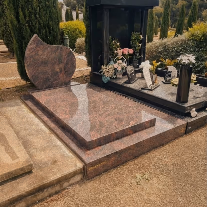 Smiling elderly man with glasses and plaid shirt sitting next to a young woman with long hair wearing a black blazer, both seated at a wooden table outdoors.