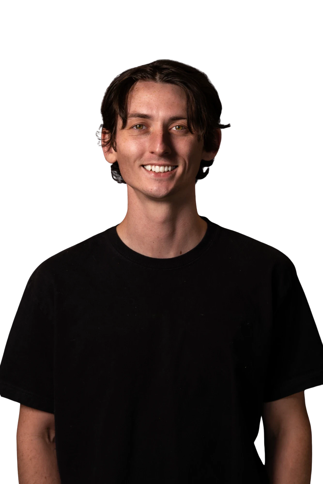 Young man with dark hair smiling, wearing a plain black t-shirt against a black background.