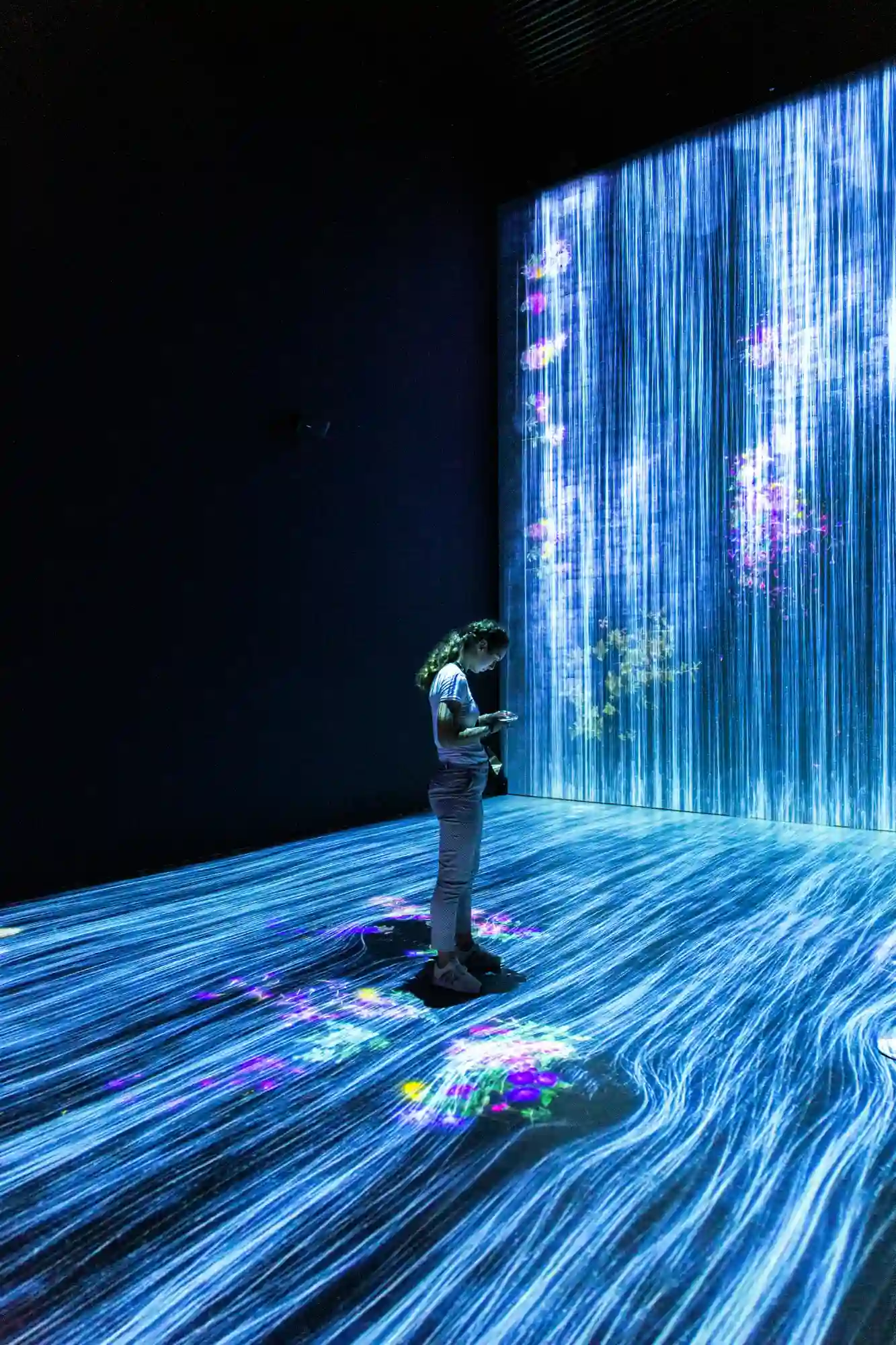 Person standing in dark room with blue light streaks and colorful floral projections on floor and wall.