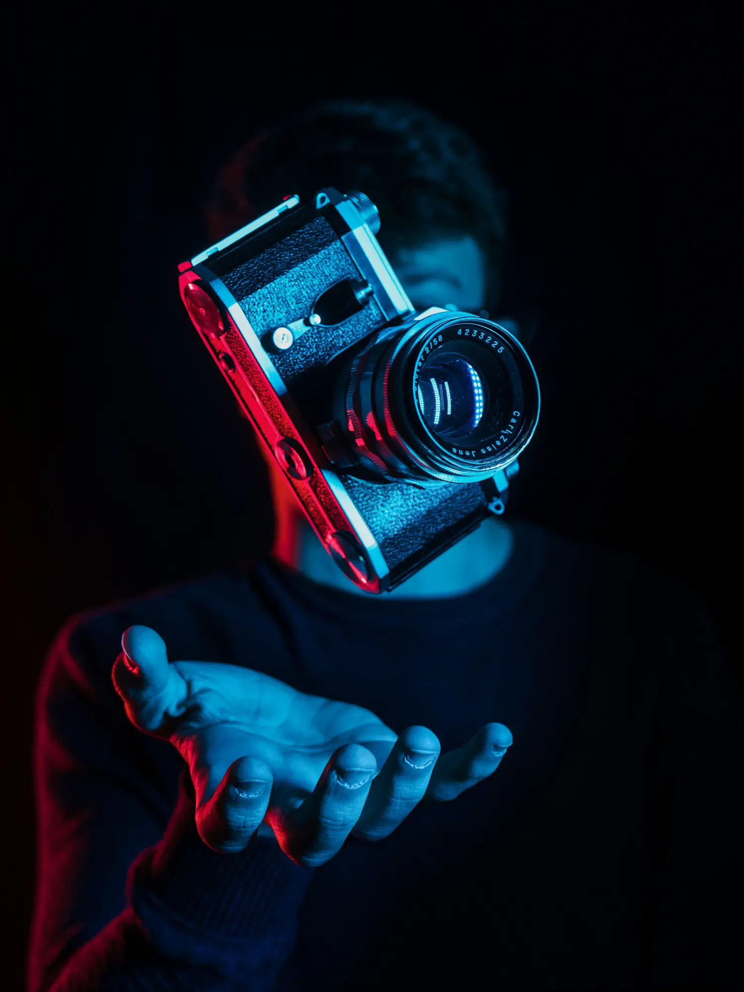 A vintage camera hovers above a person's outstretched hand in blue and red lighting.