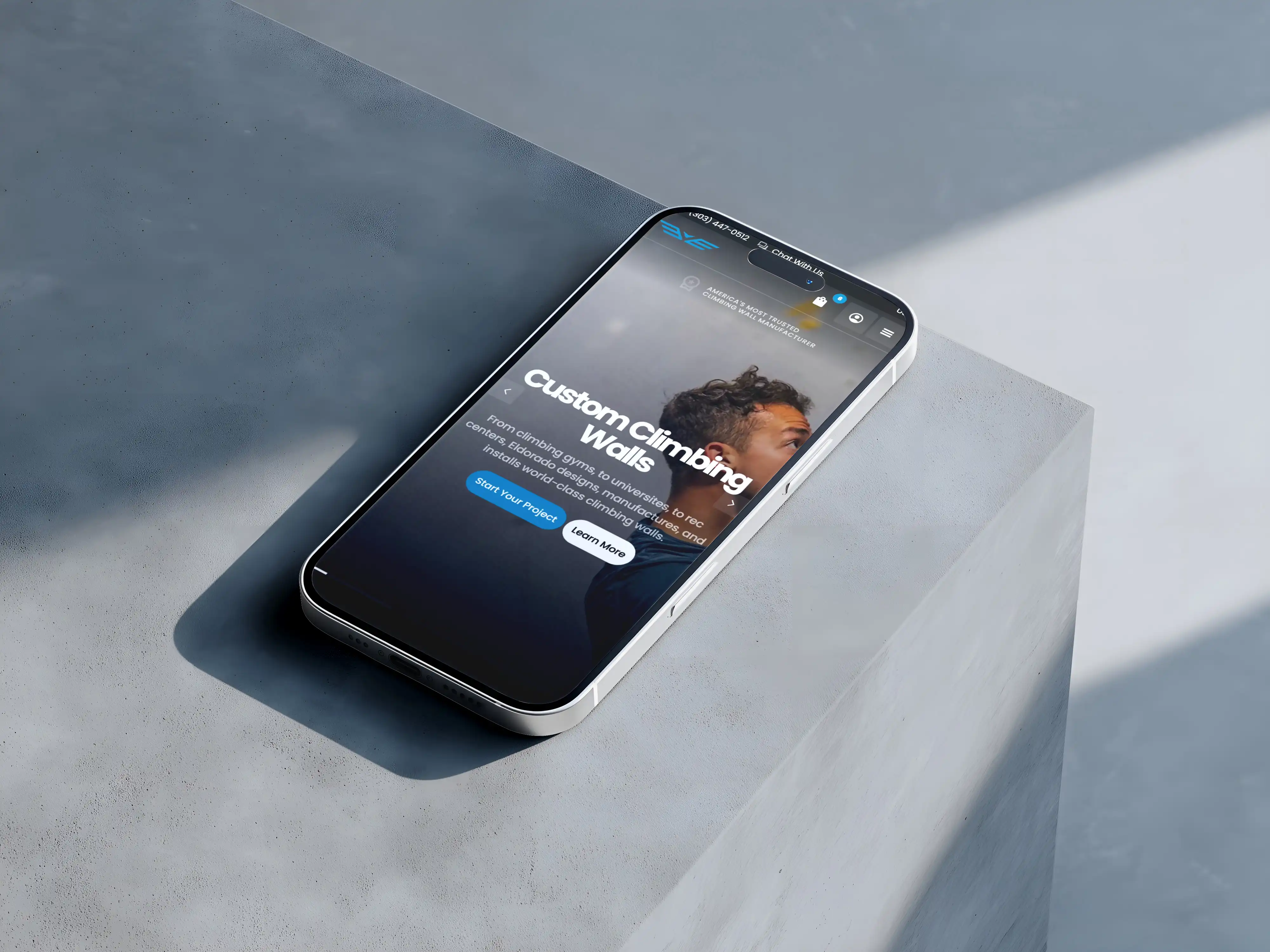 Smartphone on gray surface showing custom climbing walls website with man’s face and call-to-action buttons.
