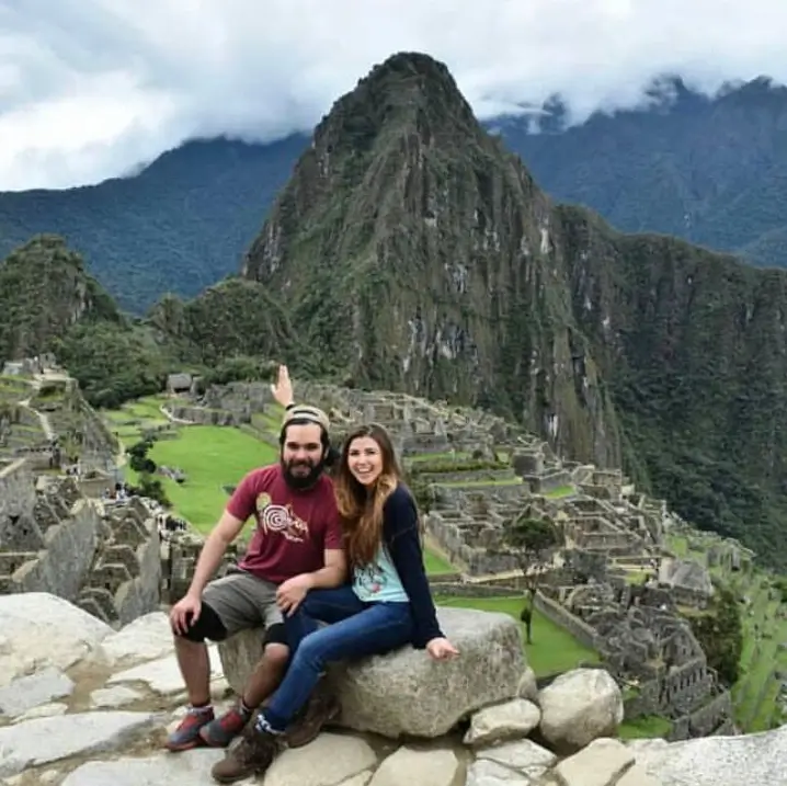 Milena y Carlos sentados en las ruinas de Machu Picchu con la montaña Huayna Picchu de fondo