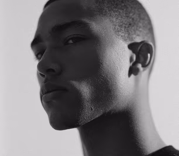 Close-up black and white portrait of a young man looking slightly sideways with shadows on his face.