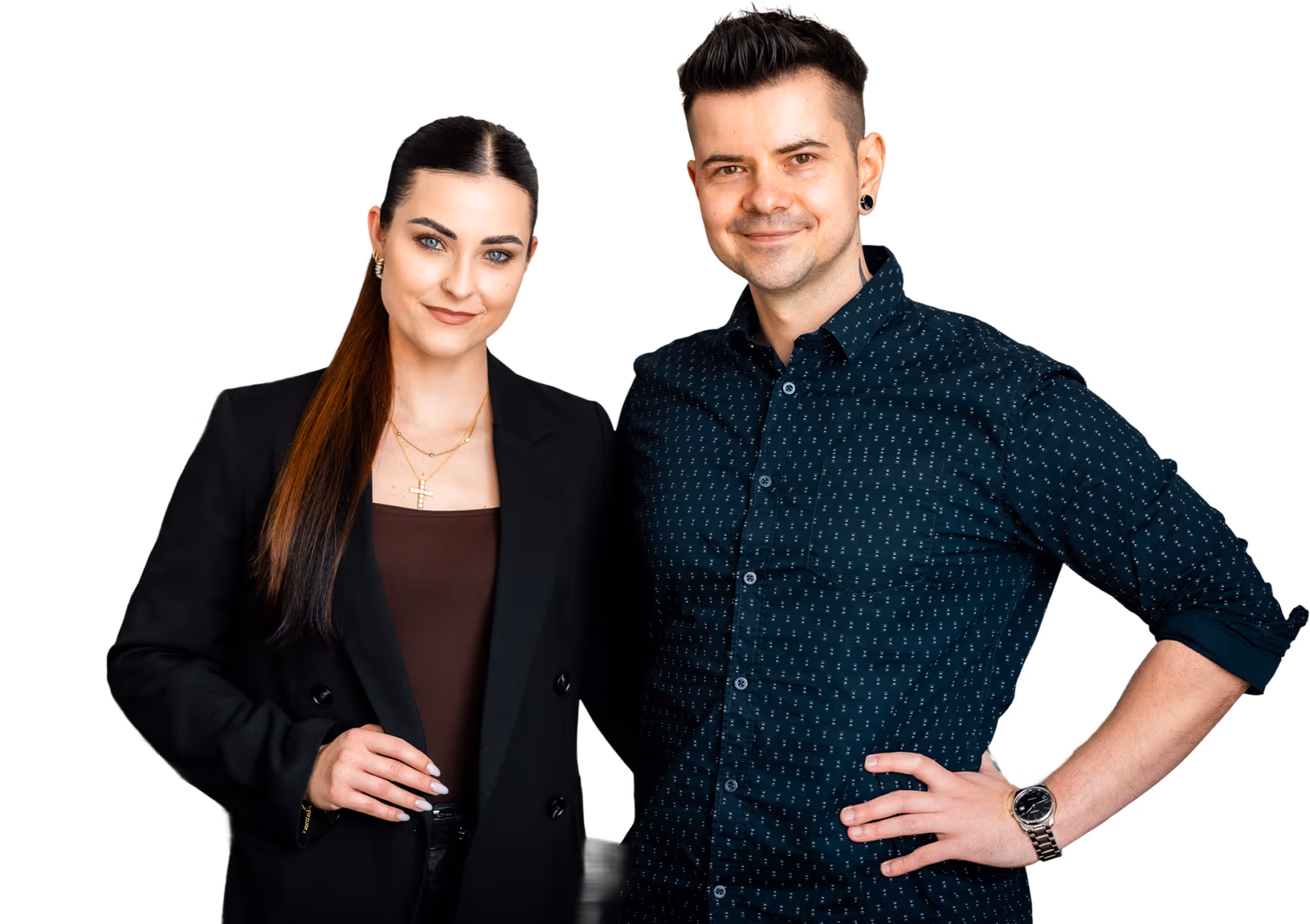 Ein lächelnder Mann und eine lächelnde Frau stehen nebeneinander; die Frau trägt einen schwarzen Blazer und der Mann ein gemustertes dunkles Hemd sowie eine Armbanduhr.