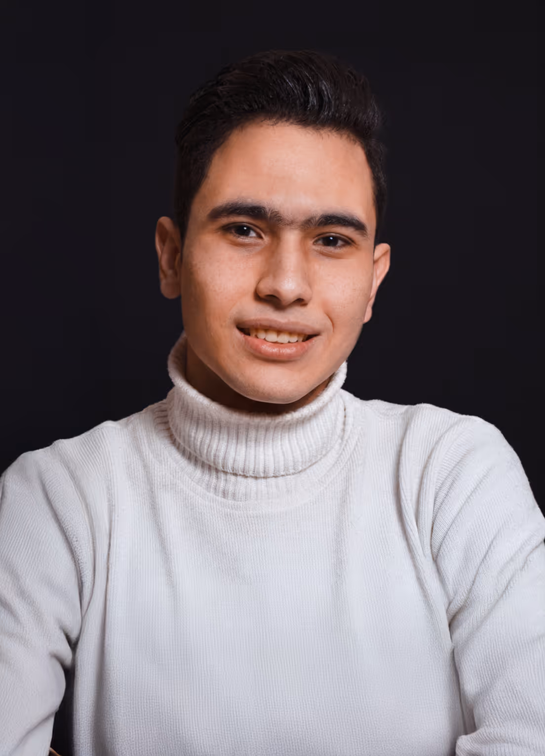 Moamen Elhawary's Portrait, young man smiling, wearing a white turtleneck sweater against a black background.