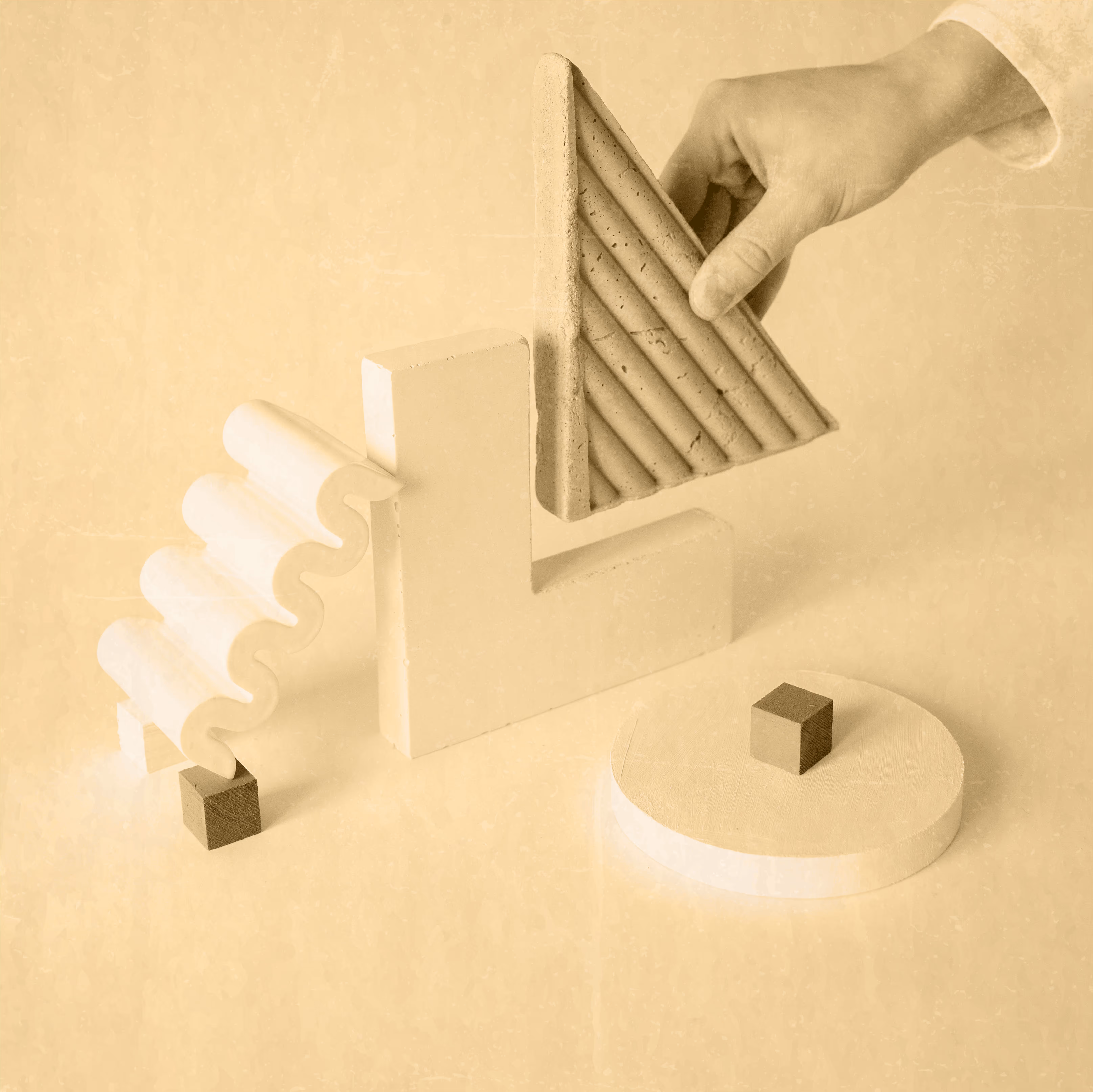 Hand holding textured triangle piece placed above white abstract geometric shapes on a neutral background.