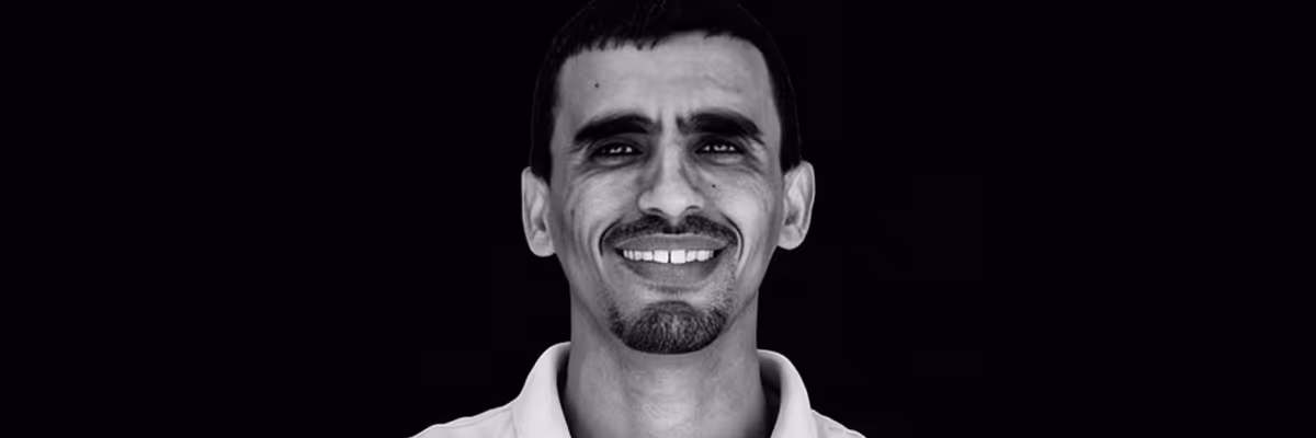 Close-up of a smiling man with short hair and a goatee against a black background.