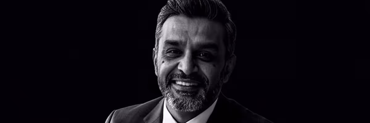Black and white portrait of a smiling man with a beard in a suit against a dark background.