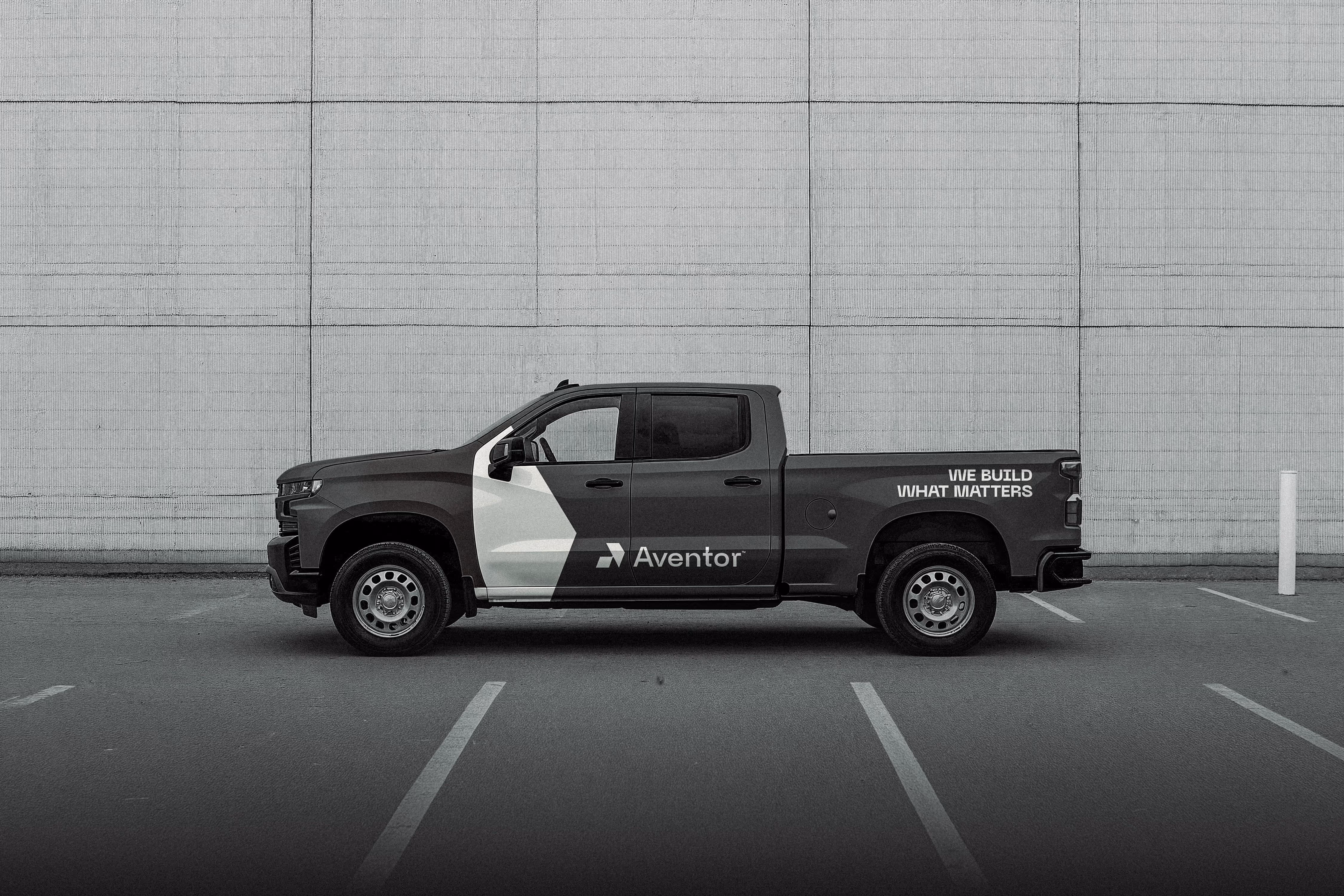Black and white pickup truck with Aventor logo and slogan parked in front of a large tiled wall.