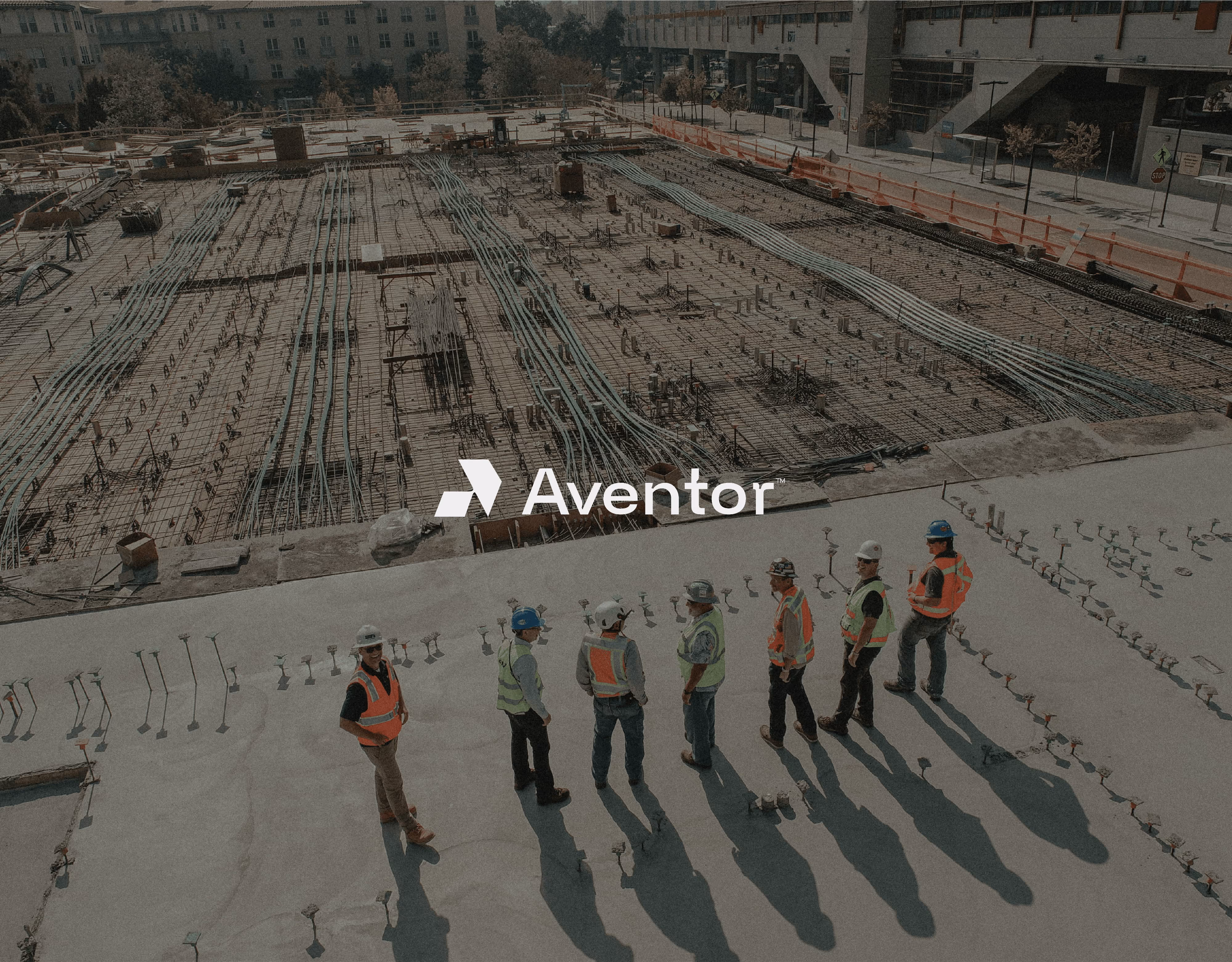 Seven construction workers in safety gear standing near a large concrete foundation at a building site.