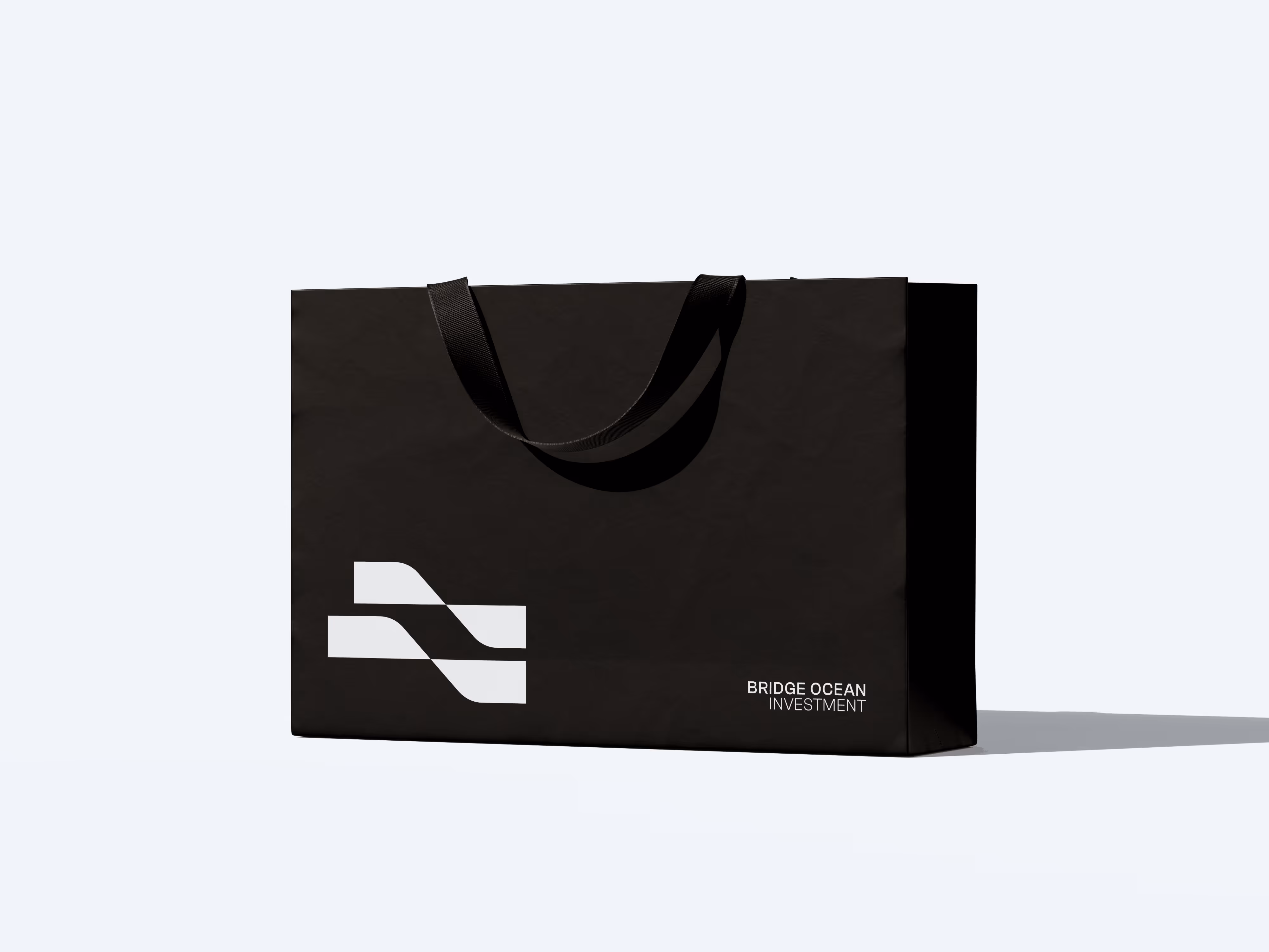 Black shopping bag with black handles and white abstract logo and text reading Bridge Ocean Investment.