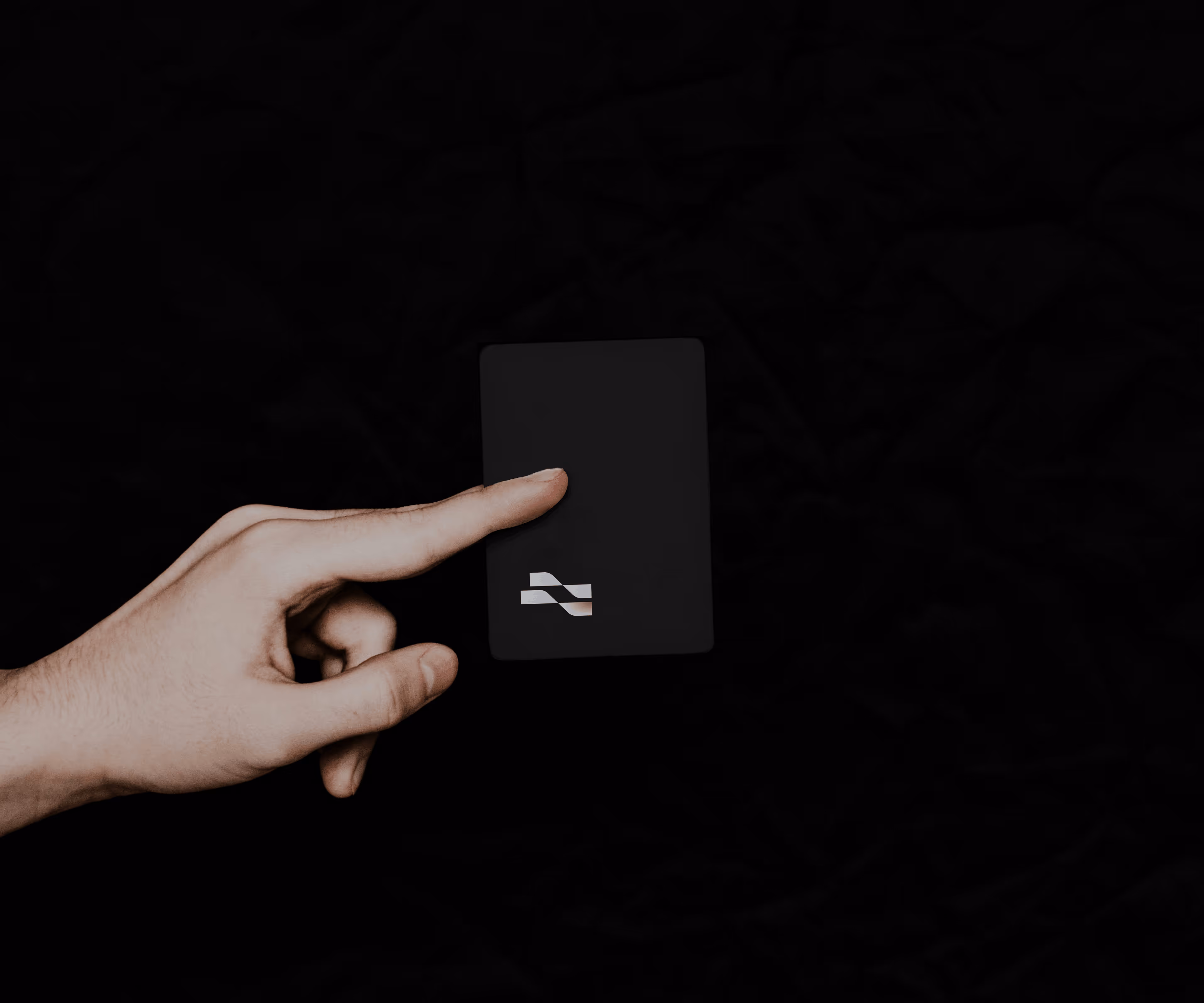 Hand pointing to a black card with a small white geometric logo on a black background.