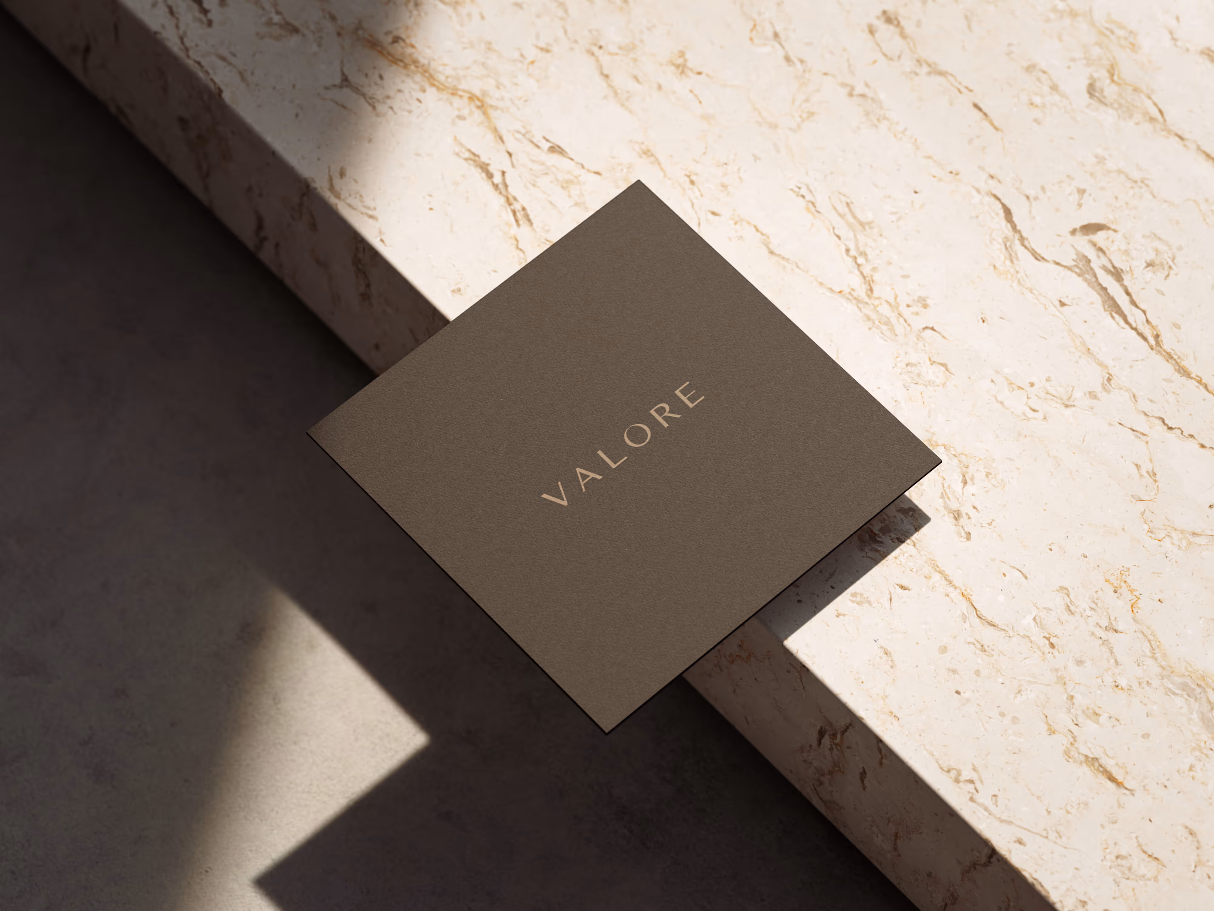 Dark gray square card with the word VALORE in gold lettering resting on a light marble surface.