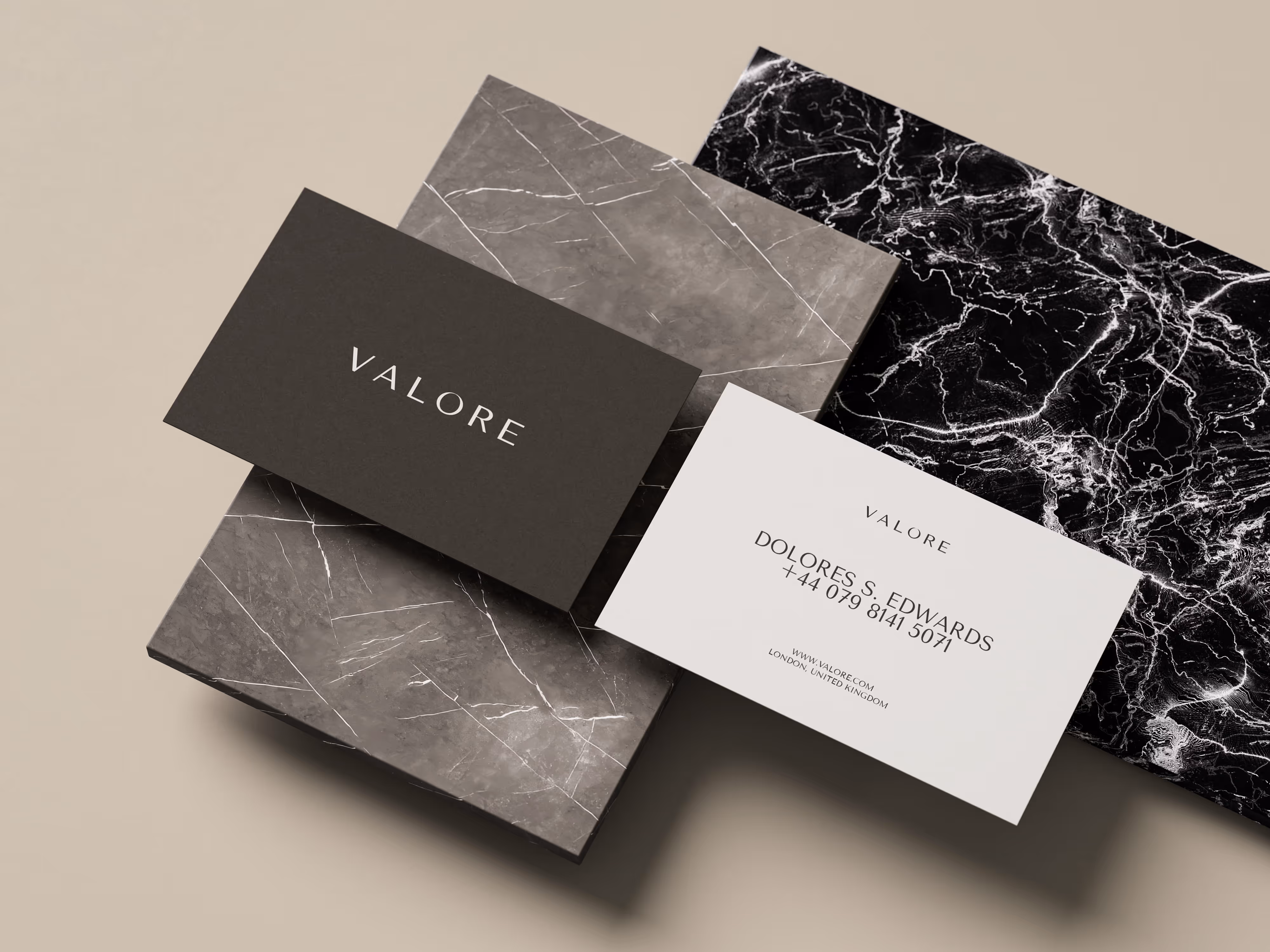 Two VALORE business cards on marble slabs; one card black with white text, the other white with contact info.