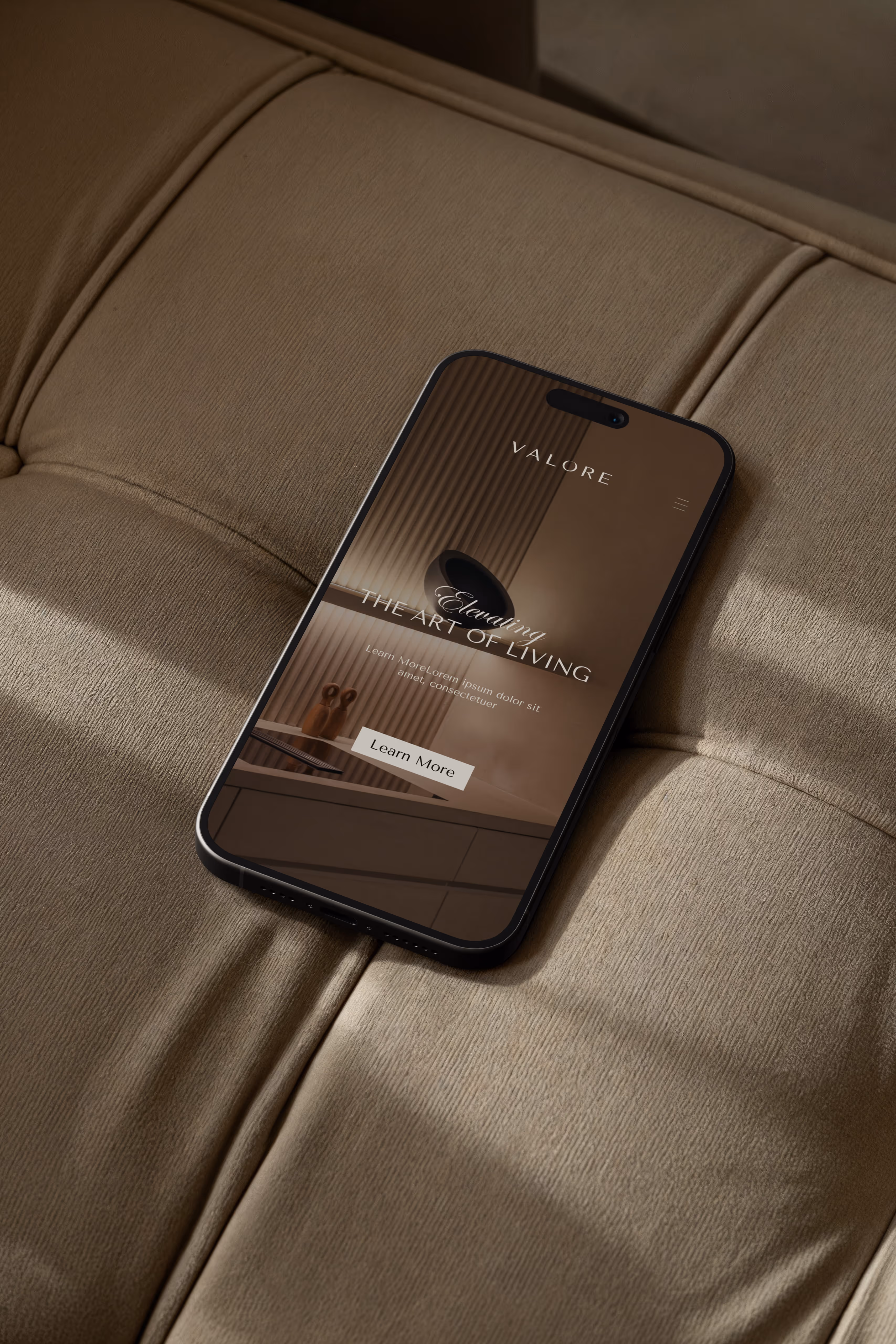 Smartphone on beige tufted fabric couch showing VALORE website with art of living theme and Learn More button.